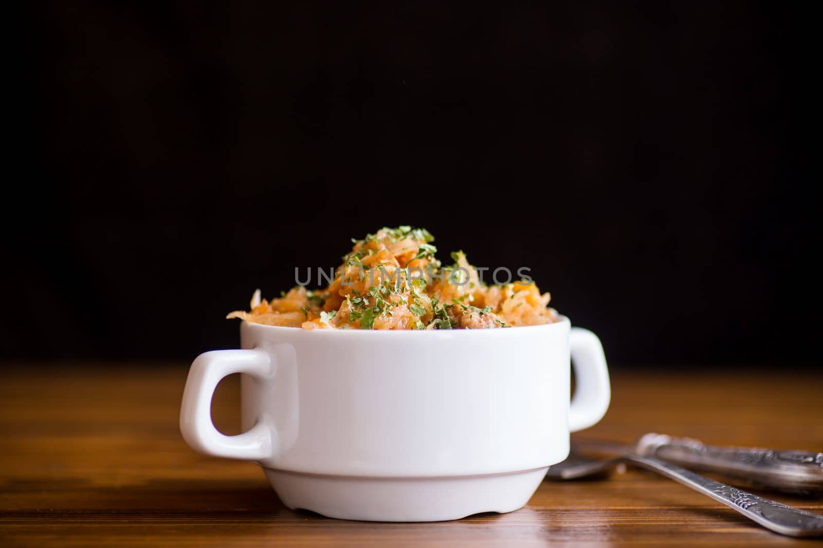 stewed cabbage with carrots and spices in a bowl on a black background.