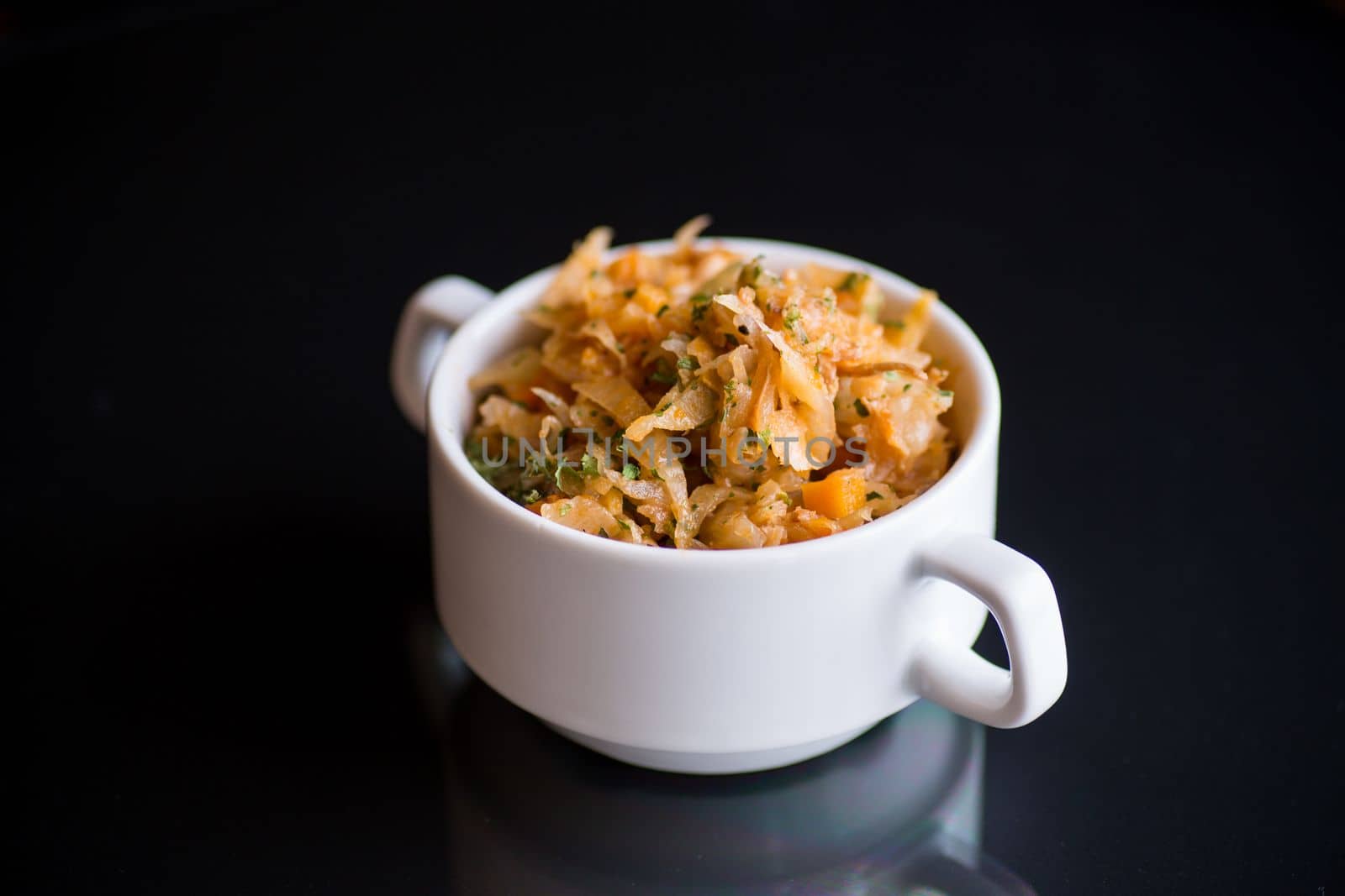 stewed cabbage with carrots and spices in a bowl on a black background.