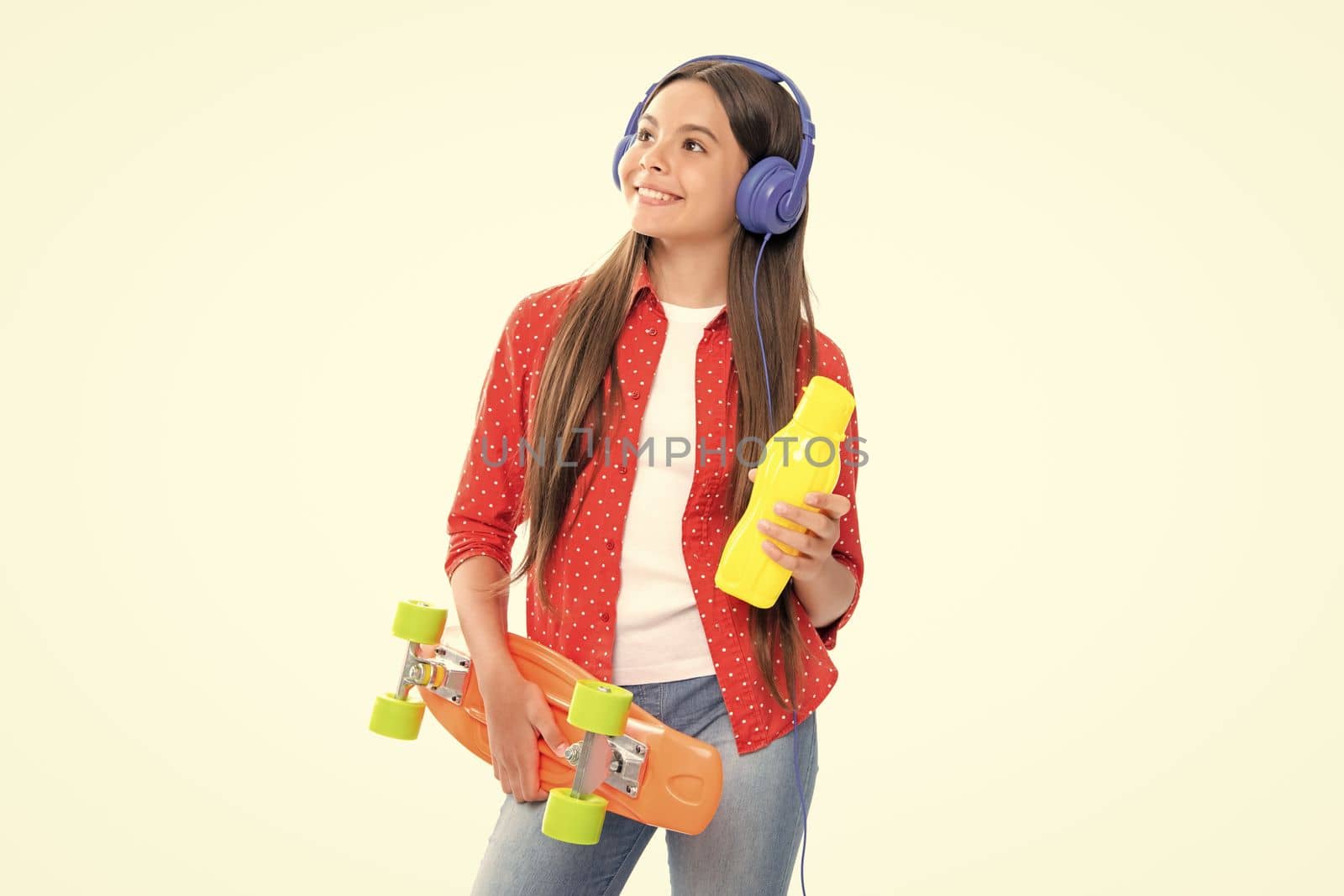 Teen girl 12, 13, 14 years old with skateboard and headphones over white studio background. Cool modern teenager in stylish clothes. Teenagers lifestyle, casual youth culture