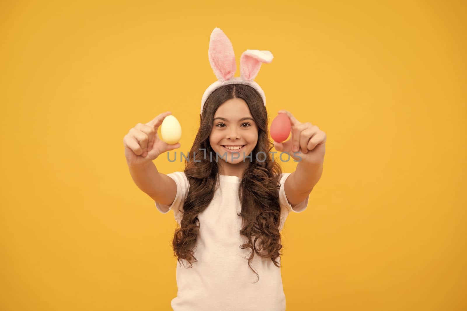 smiling kid in bunny ears hold eggs on yellow background, easter by RedFoxStudio