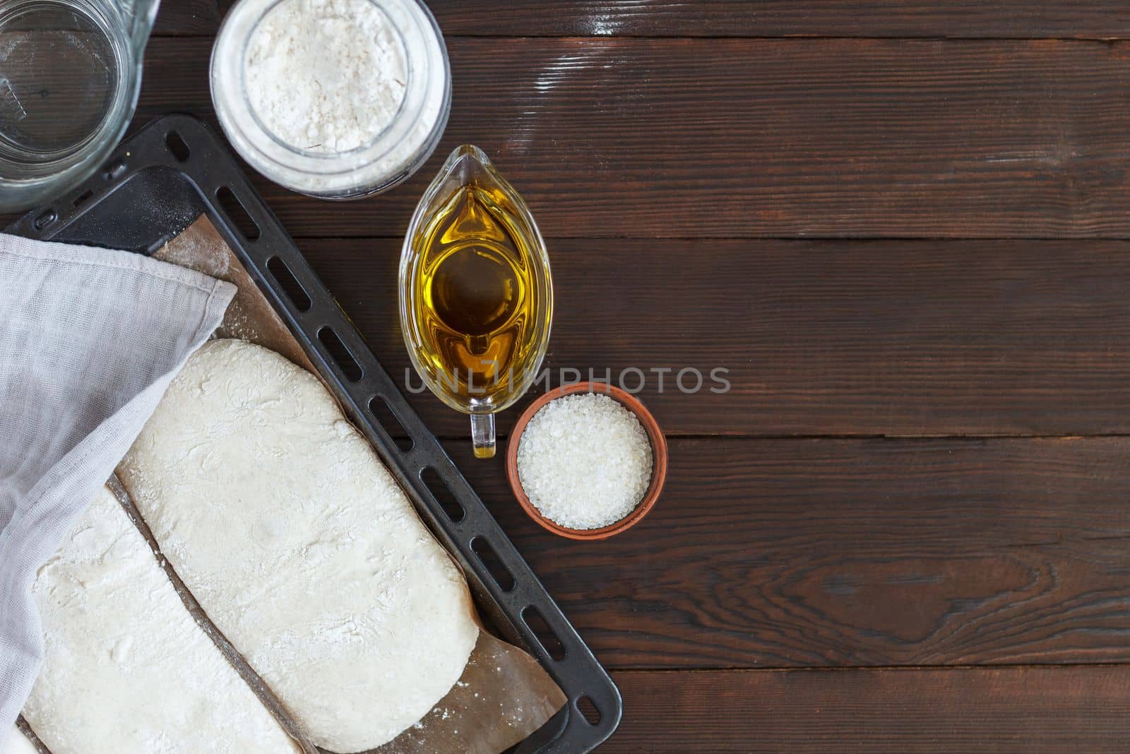 fresh raw dough for baking bread on a baking sheet, ready for baking with ingredients: flour, olive oil, water, salt on a wooden background. by lara29