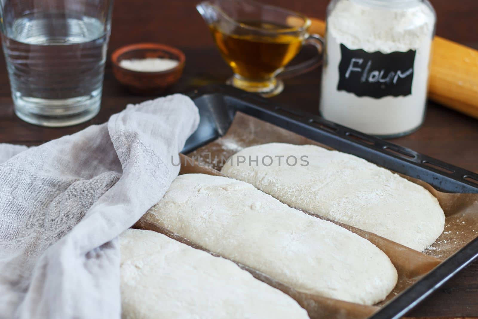 fresh raw dough for baking bread on a baking sheet, ready for baking with ingredients: flour, olive oil, water, salt on a wooden background. by lara29