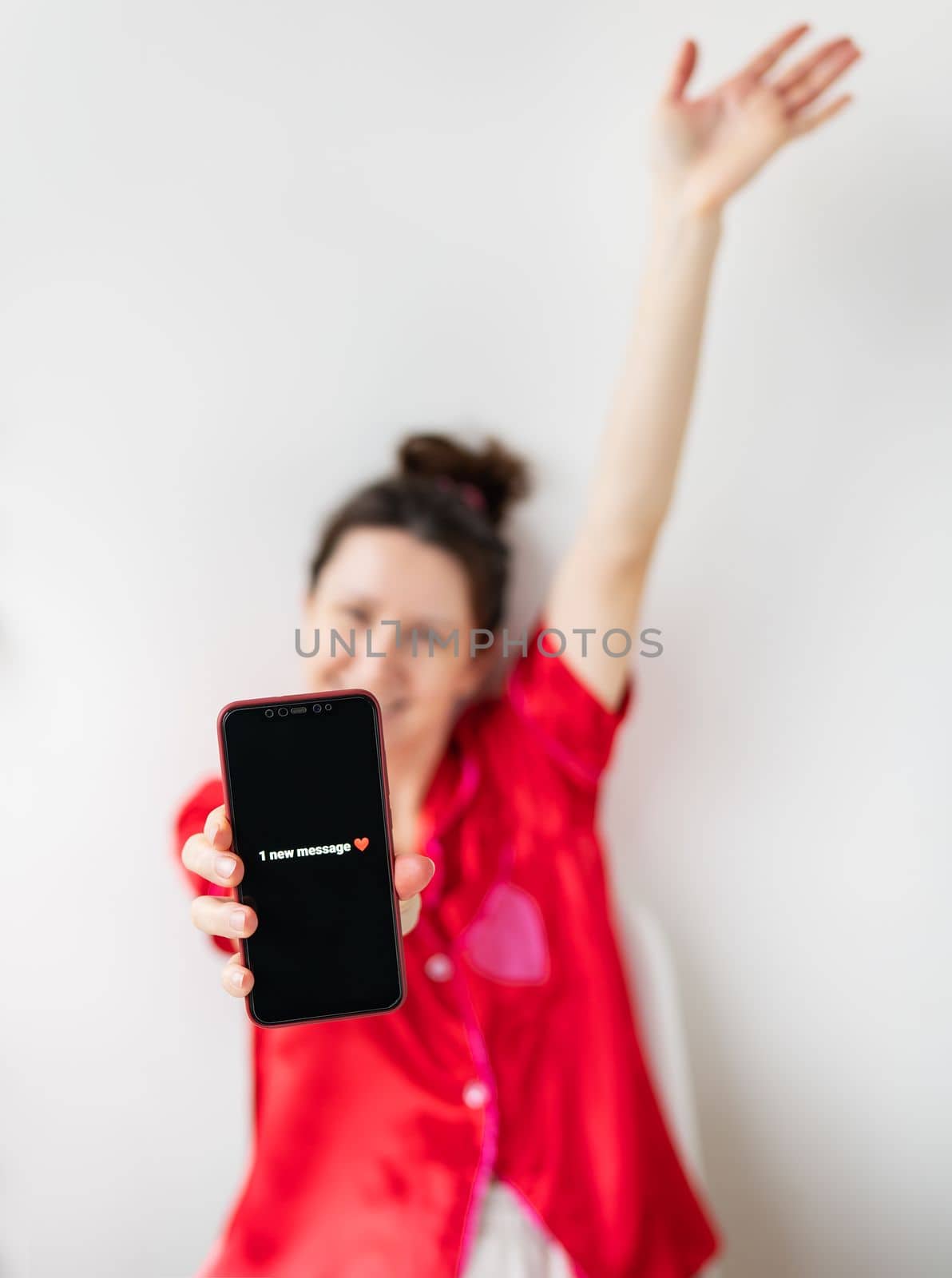 A happy girl is holding a smartphone with an activated screen with 1 SMS message in the shape of a heart. Concept of Valentine's Day, February 14