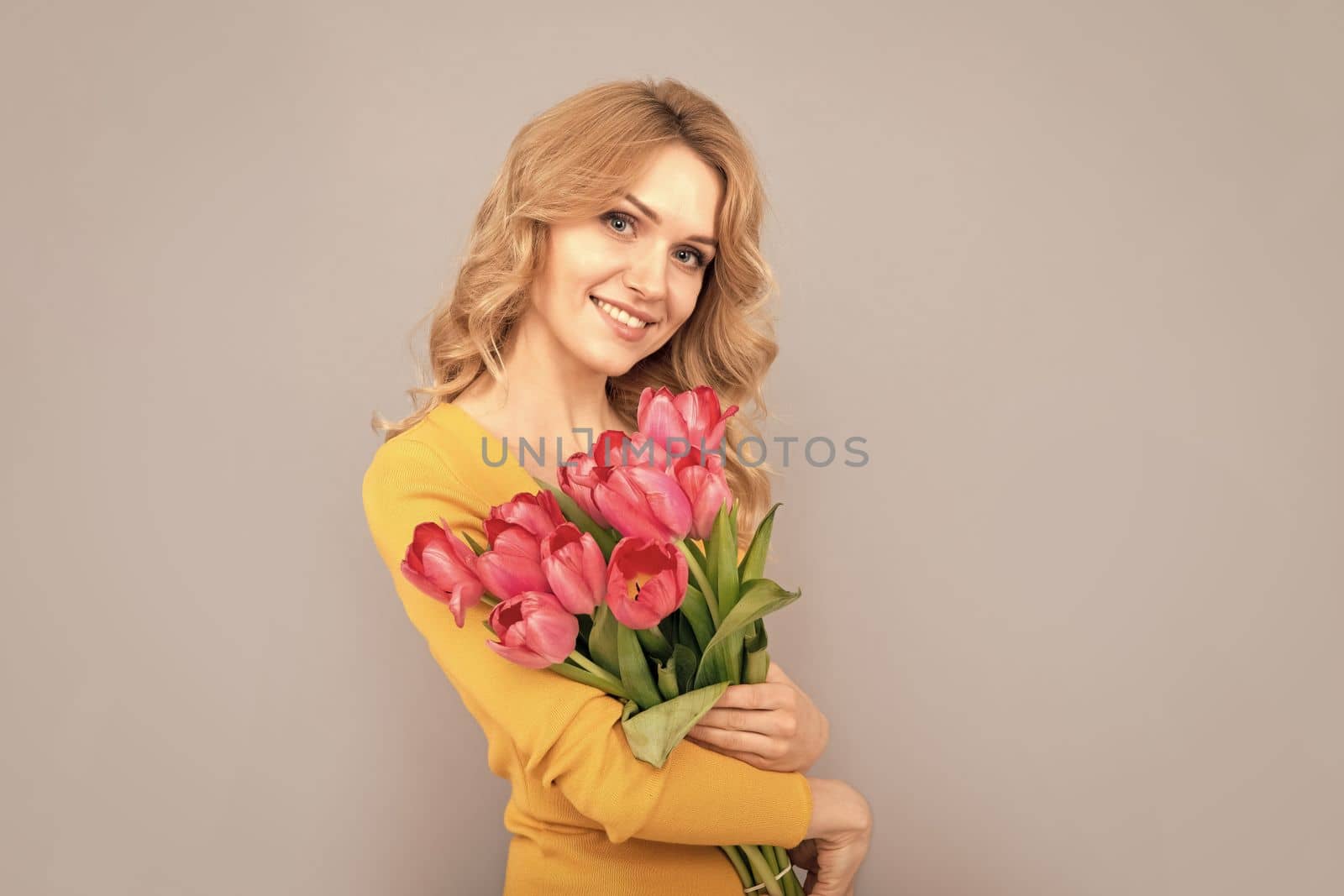 positive woman with tulips. lady hold flowers for spring holiday. girl with bouquet on grey background. floral present for womens day. 8 march and mothers day.