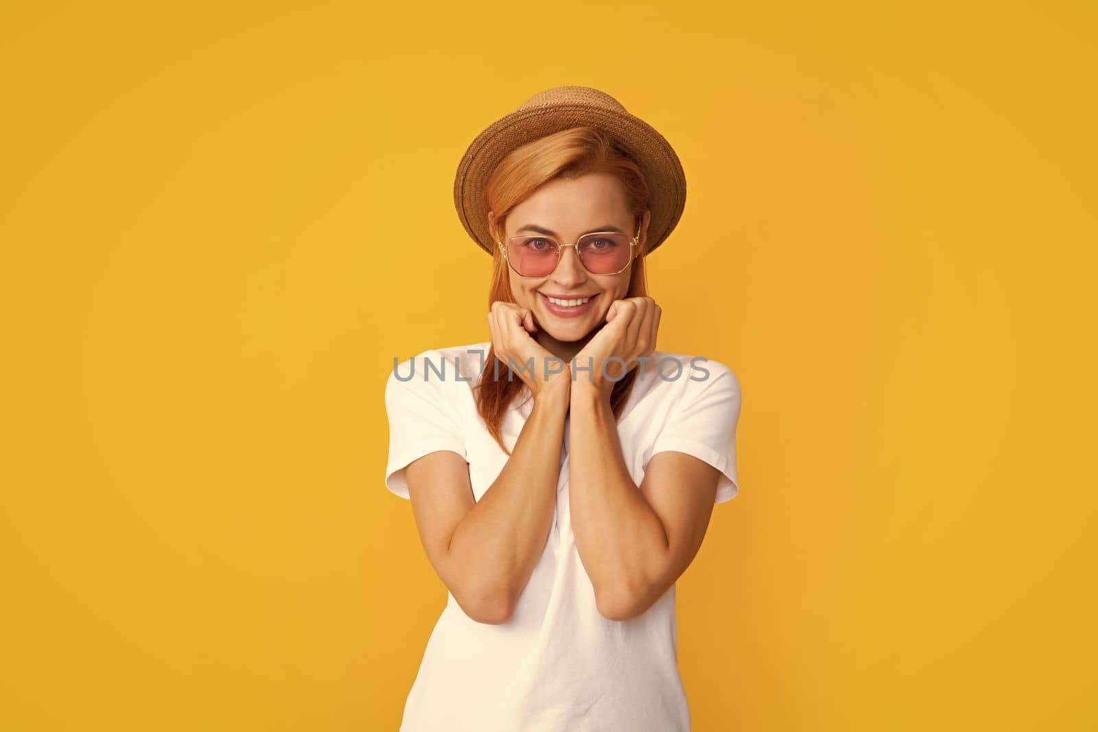 Smiling portrait of pretty young woman wearing sunglasses and straw hat over yellow background. Happy girl enjoying summer