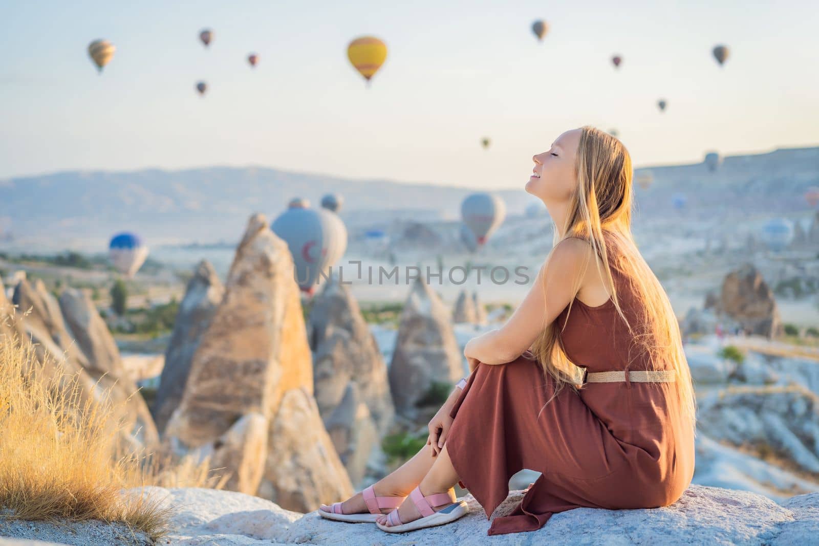 Tourist woman looking at hot air balloons in Cappadocia, Turkey. Happy Travel in Turkey concept. Woman on a mountain top enjoying wonderful view.