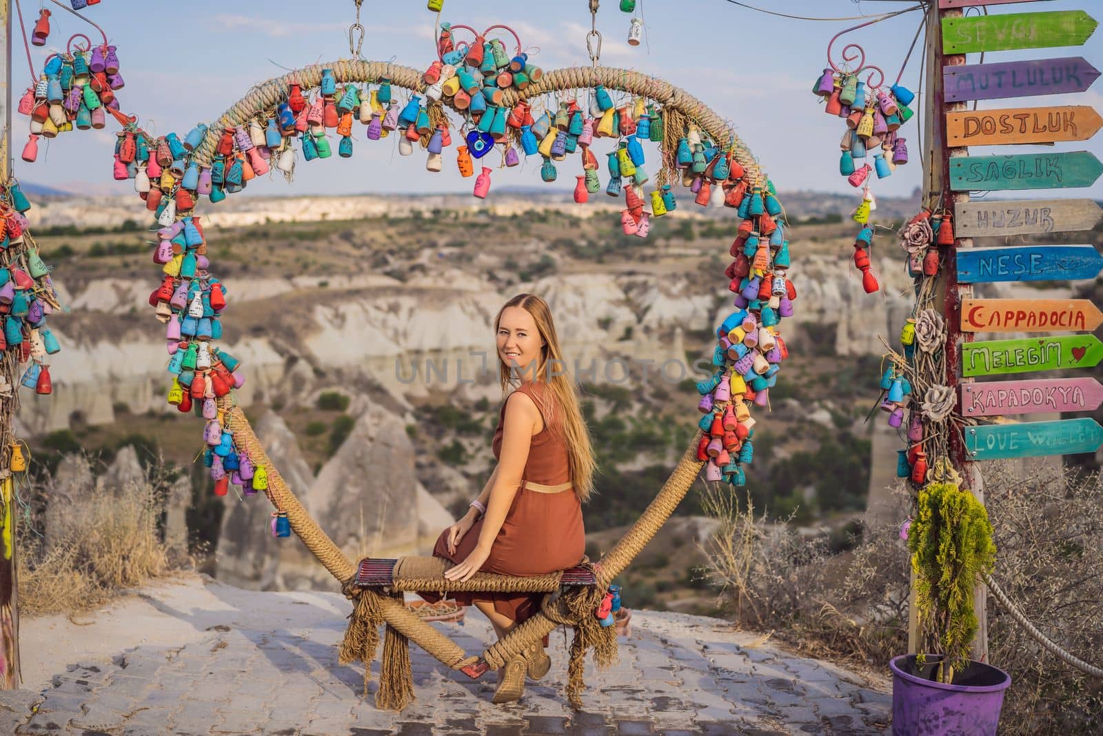 Young woman exploring valley with rock formations and fairy caves near Goreme in Cappadocia Turkey. Wish tree. Small multi-colored jugs with inscriptions, wishes hanging on the branches of a tree., against the backdrop of sand ruins and blue sky.