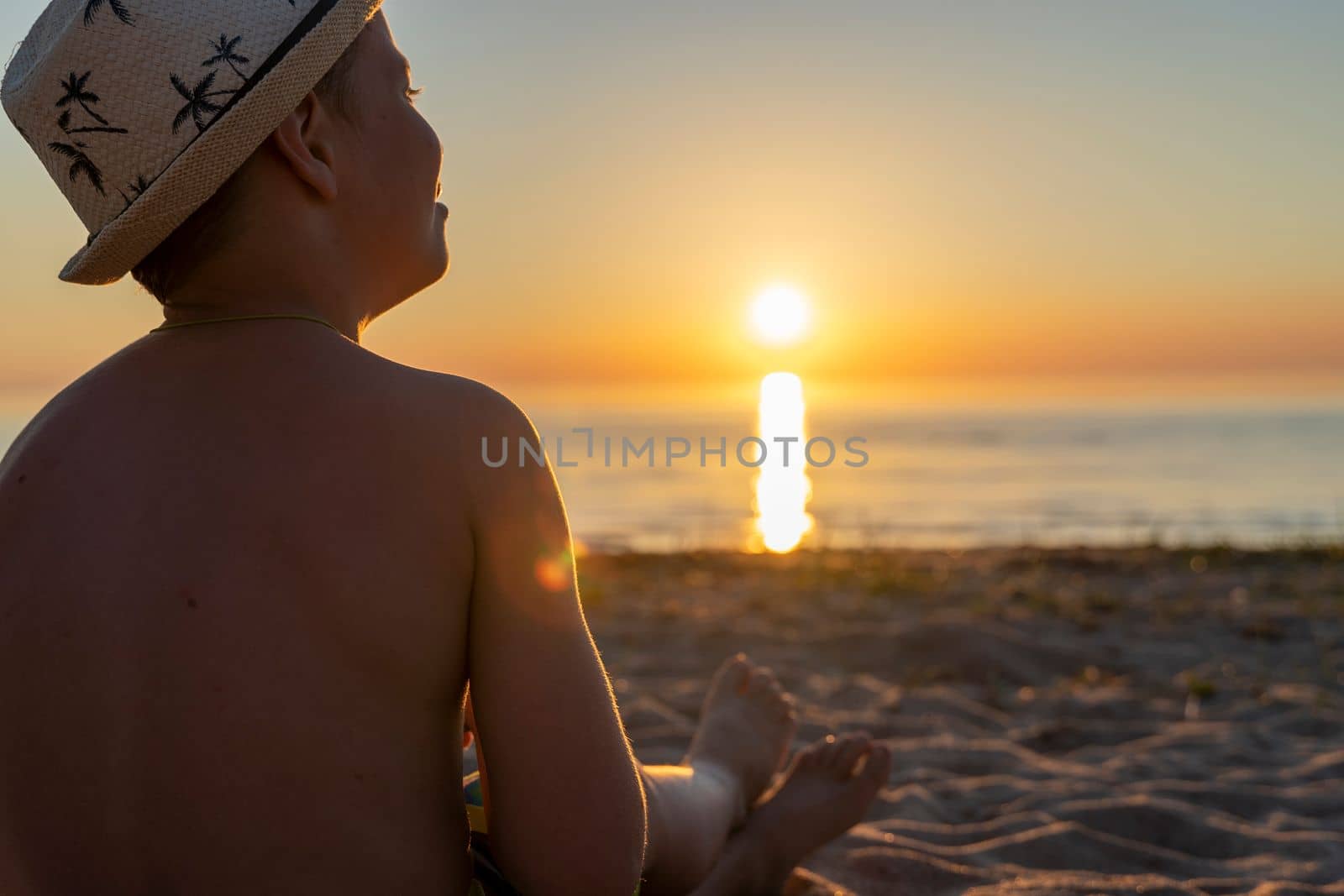 a happy boy in a sun hat who sits on the beach at sunset and dreams. Childhood dreams, family happiness, vacation at sea