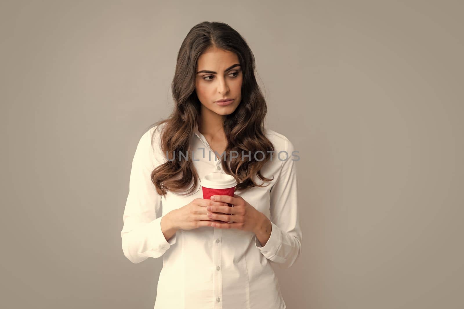Portrait of a beautiful young woman with a cup of coffee standing on the gray background