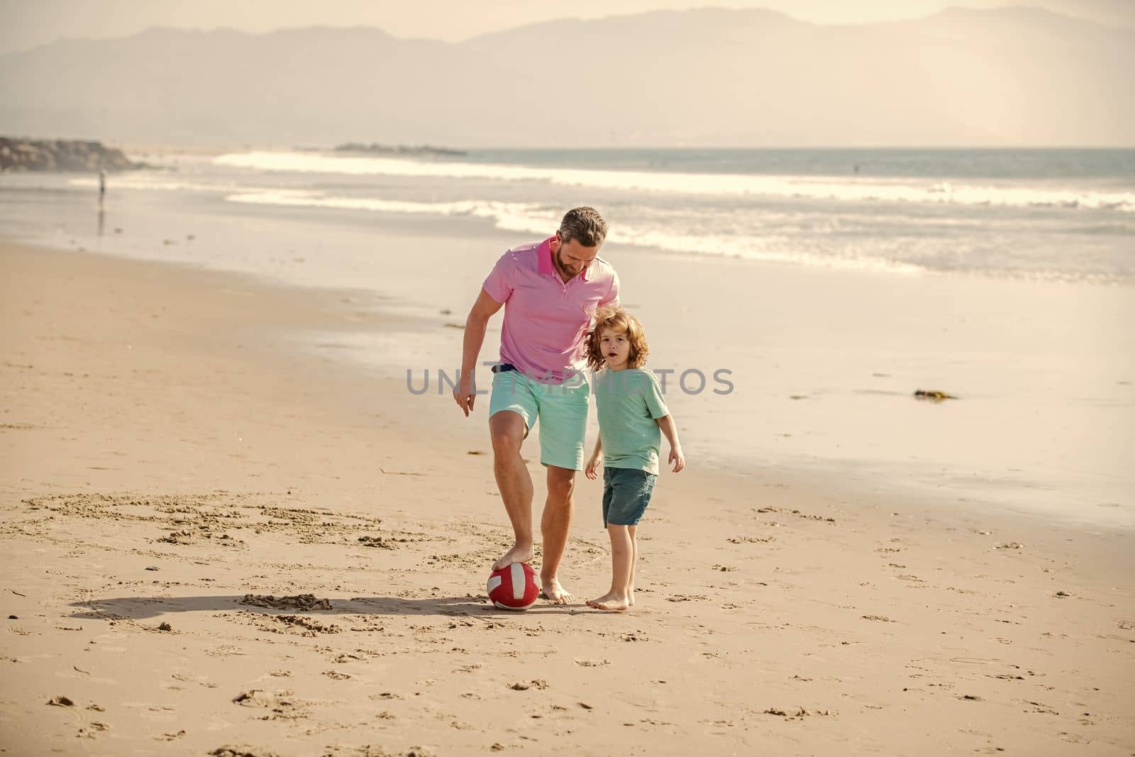 cheerful kid and dad running on beach in summer vacation with ball, friendship.
