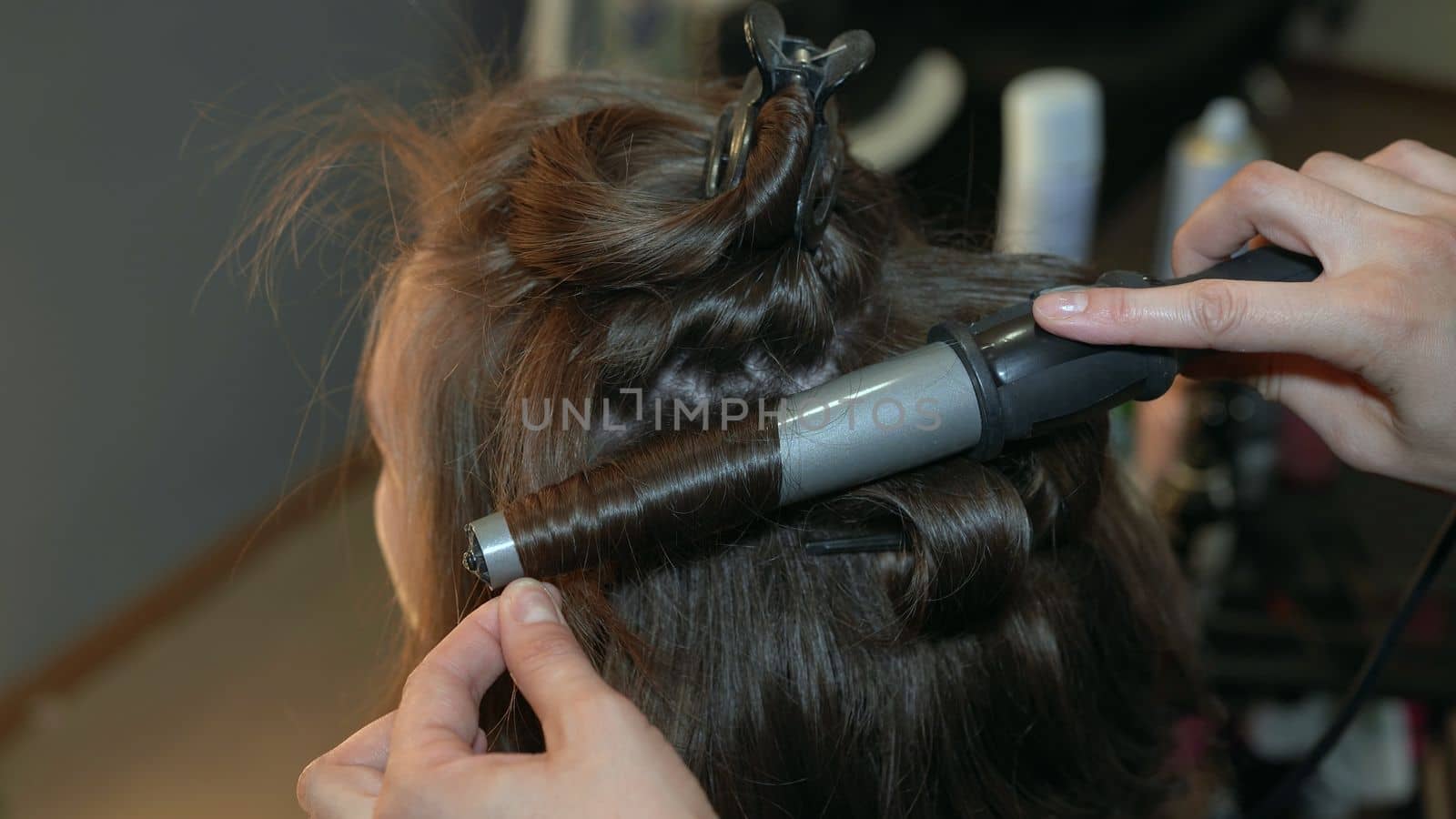 The hairdresser curls the hair of a girl in a beauty salon using a curling iron