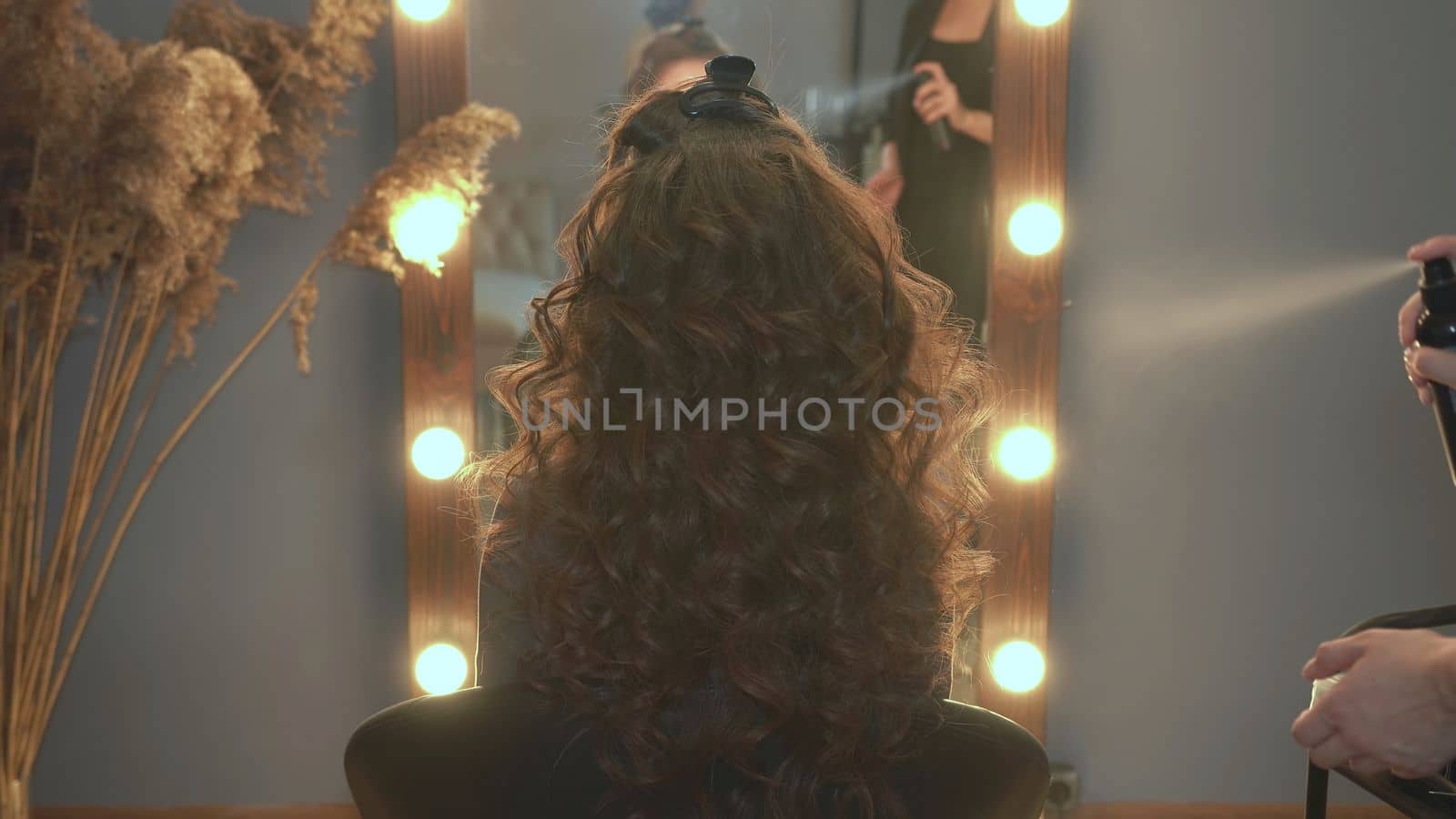 The hairdresser fixes curly hair with hairspray
