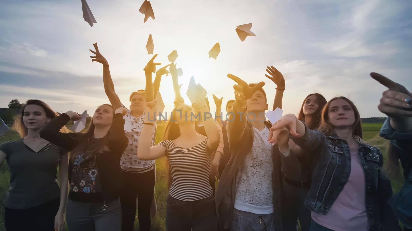 Happy friends launch paper airplanes at sunset