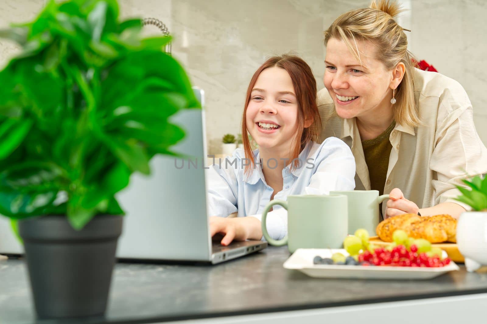 Happy mother and daughter having breakfast in kitchen and using digital devices. Lifestyle by PhotoTime