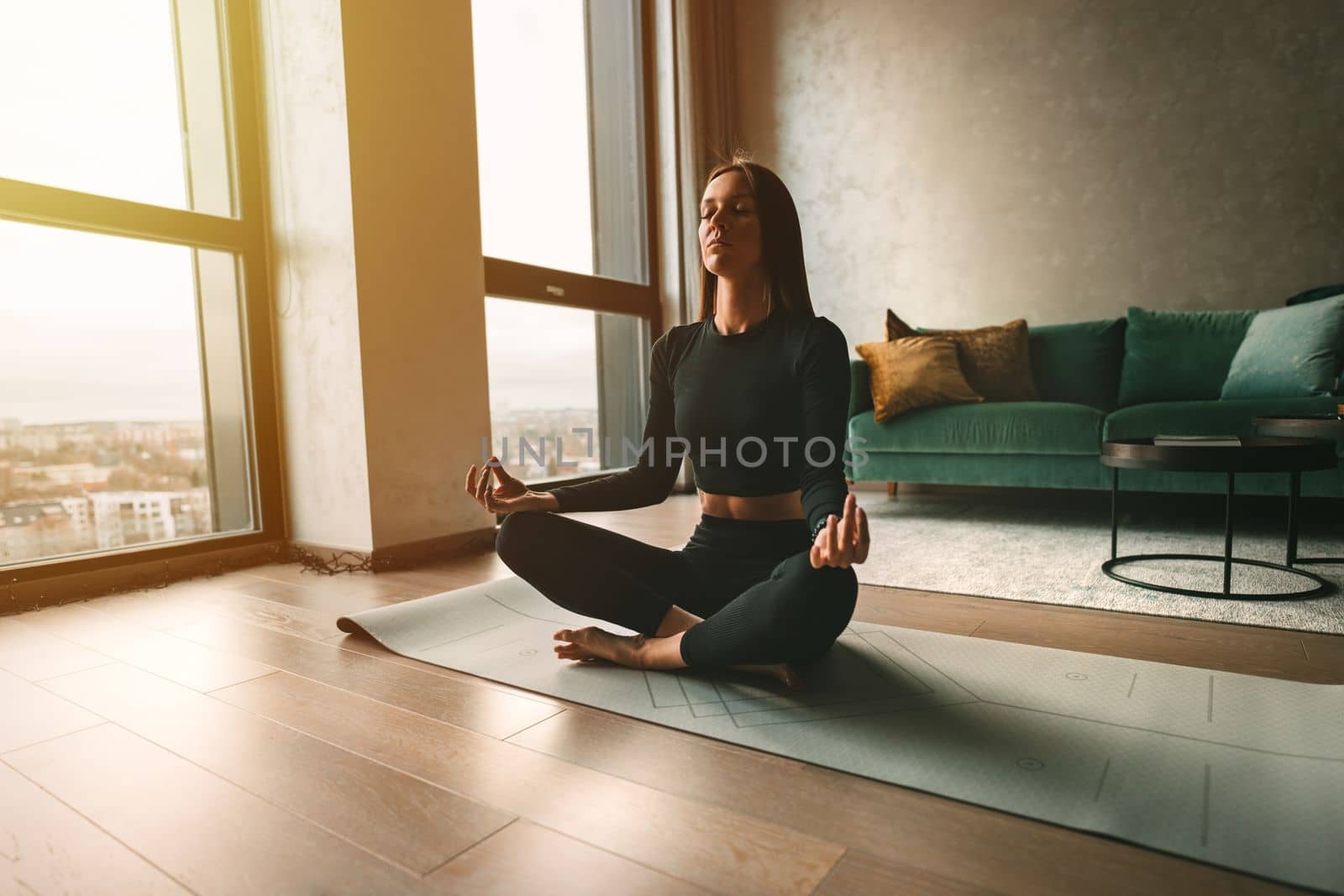 Woman practices yoga and meditates with eyes closed at home. Calmness and appeasement concept. Woman sitting in easy pose or sukhasana with mudra. by DariaKulkova