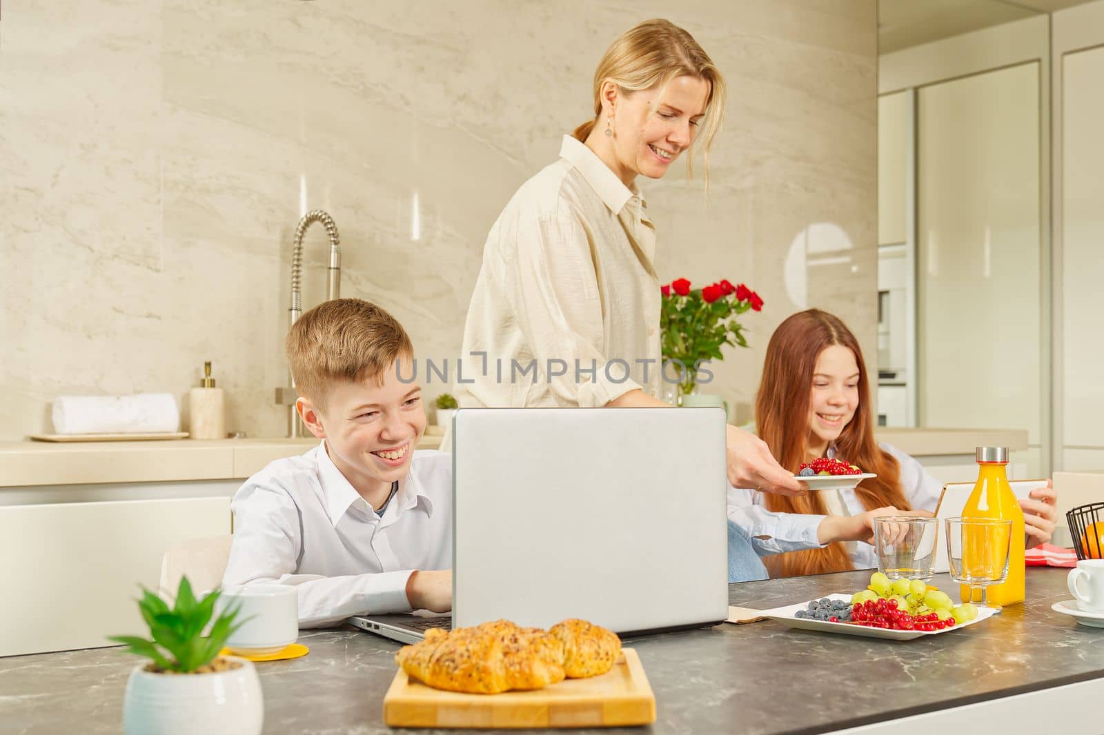 Young family with school kids have fun at breakfast time. Happy family eating healthy breakfast. Quality time with Family in kitchen eating together. Family Using Digital Devices At Breakfast