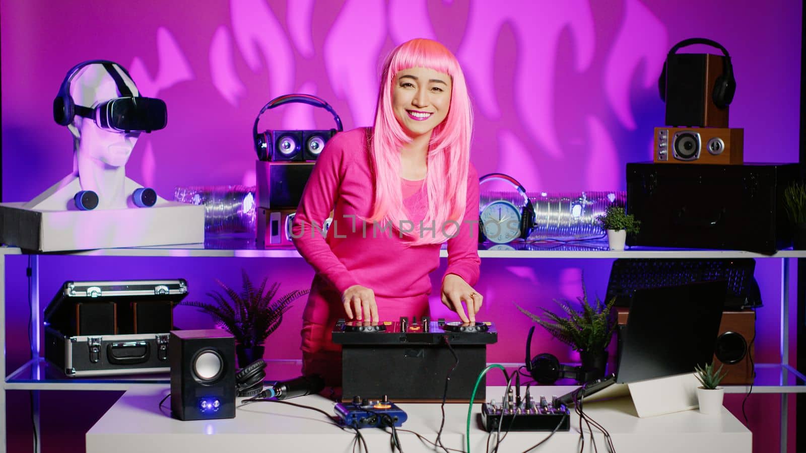 Asian musician standing at dj table mixing electronic sound with techno creating new remix, having fun in club during night time. Smiling performer playing at professional mixer during evening party
