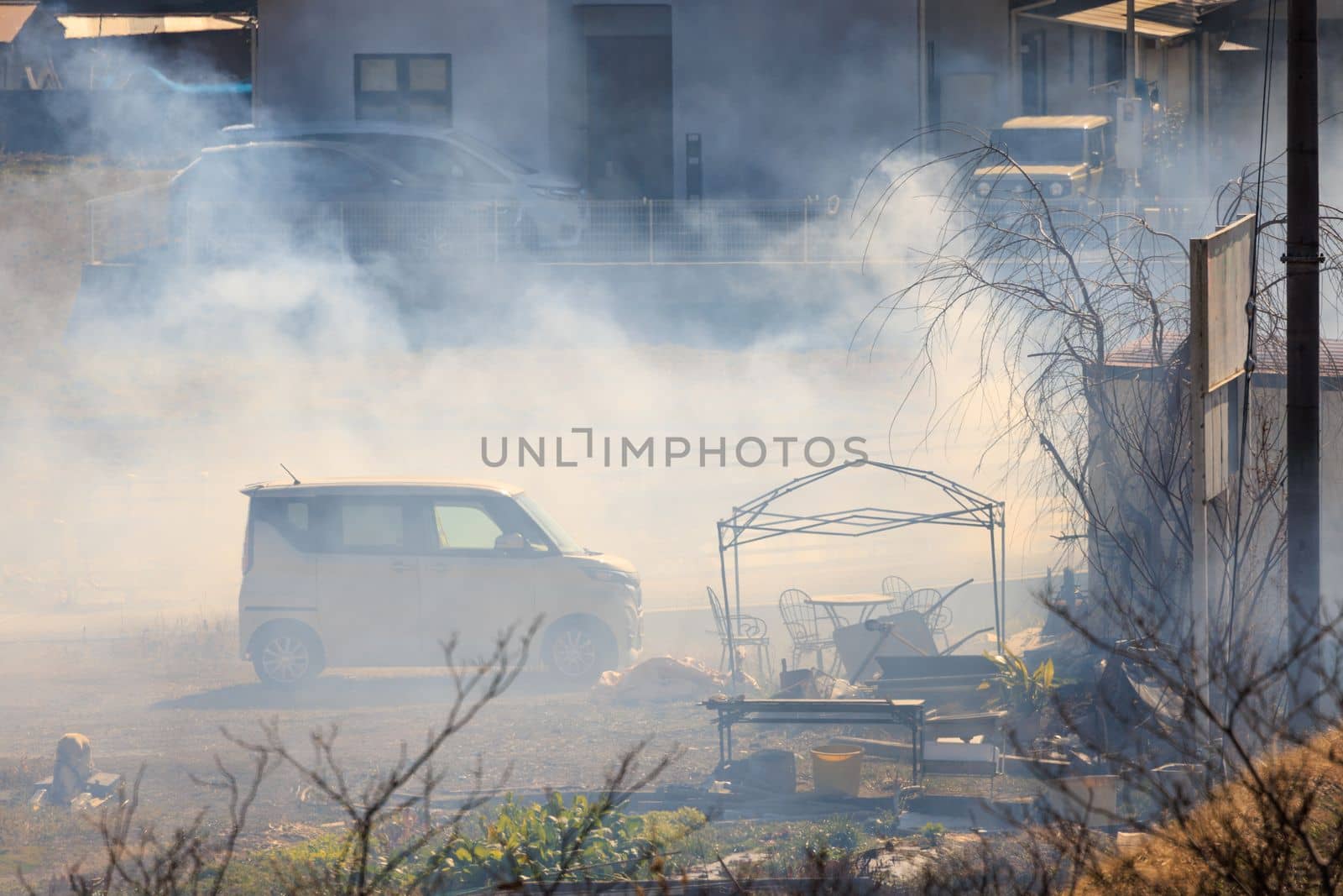 Thick smoke around small car on suburban yard with garden furniture by Osaze