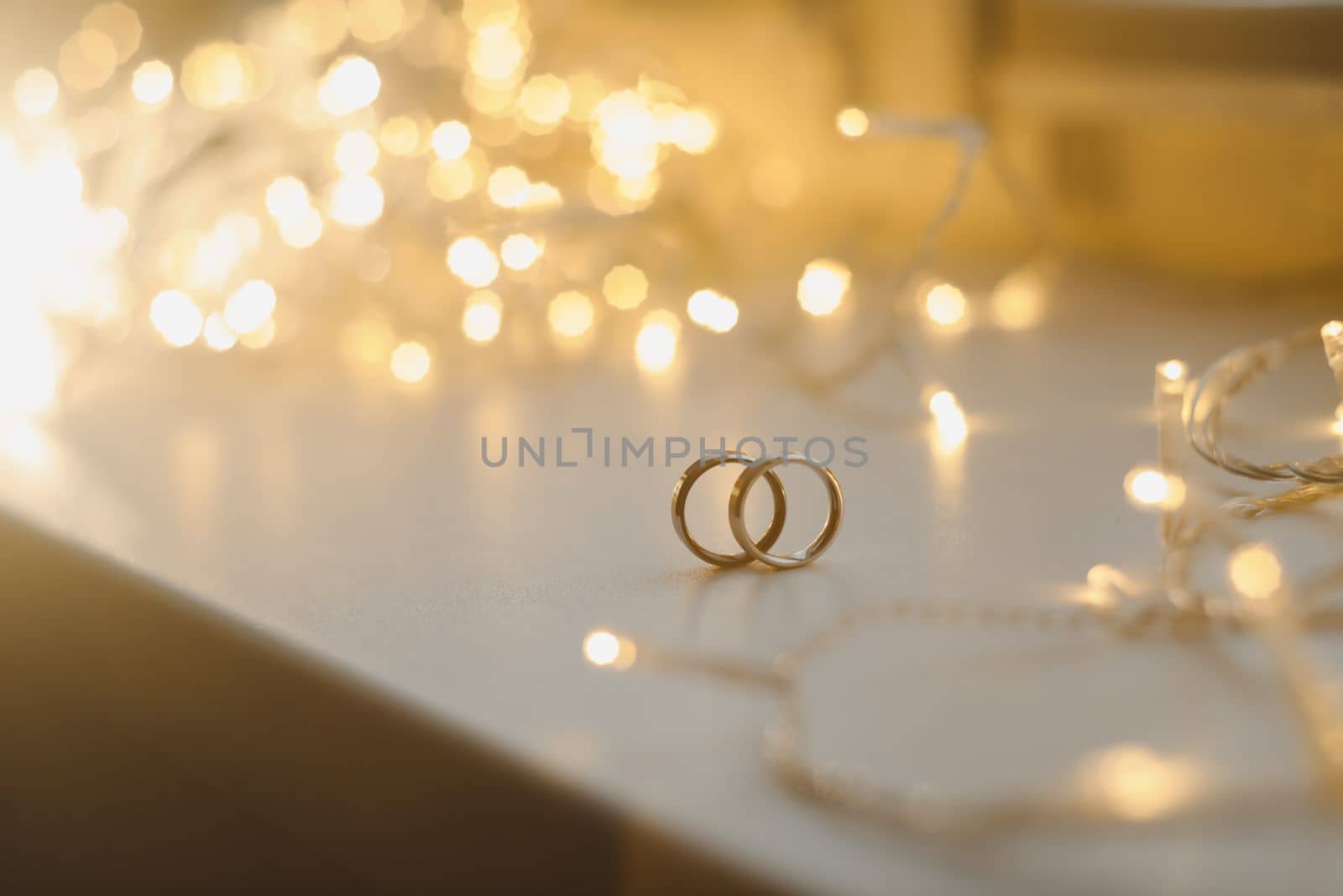 Wedding rings on blured bokeh glowing golden background. Symbol of love and romance on a textured glitter background with copy space for your greeting or congratulations.