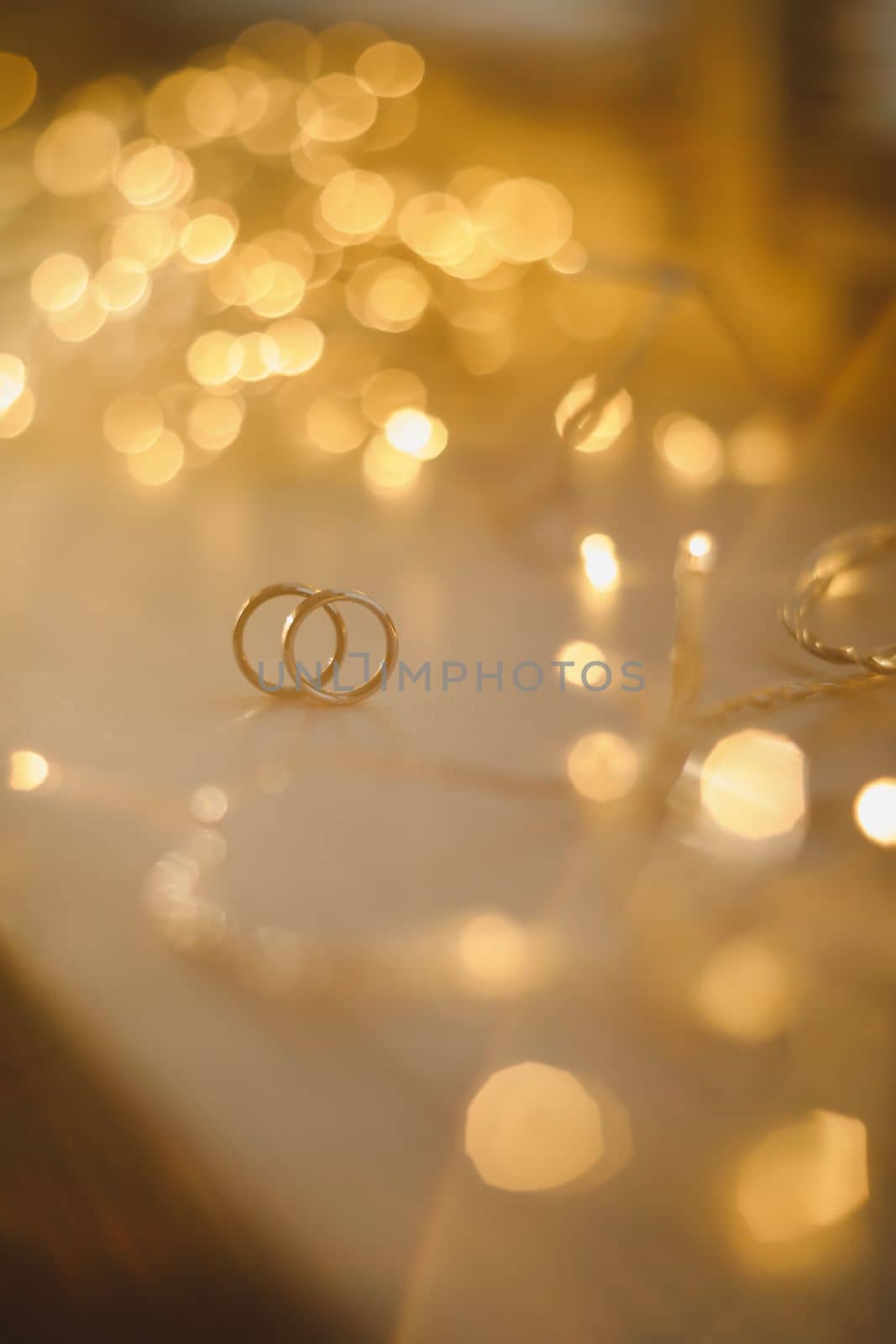 Wedding rings on blured bokeh glowing golden background. Symbol of love and romance on a textured glitter background with copy space for your greeting or congratulations.