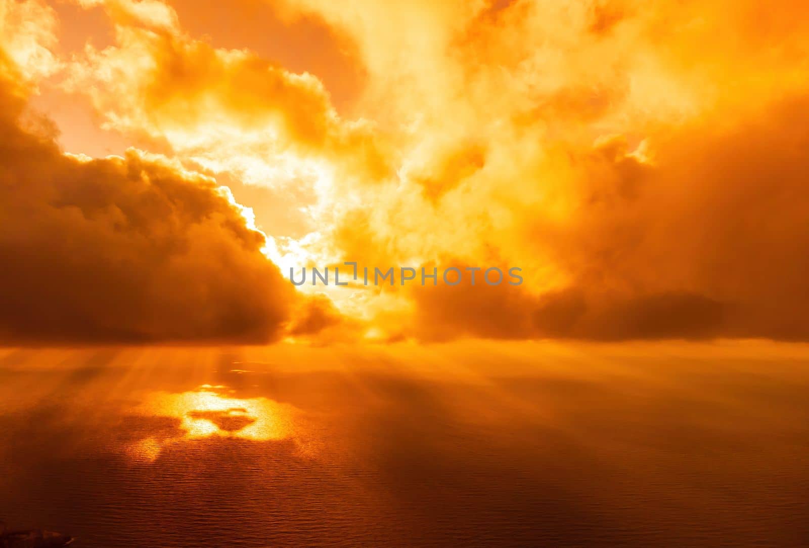 A red burning sunset with the silhouette of a cliff over the sea. Abstract nature summer or spring ocean sea background. Small waves on golden warm water surface with bokeh lights from sun.