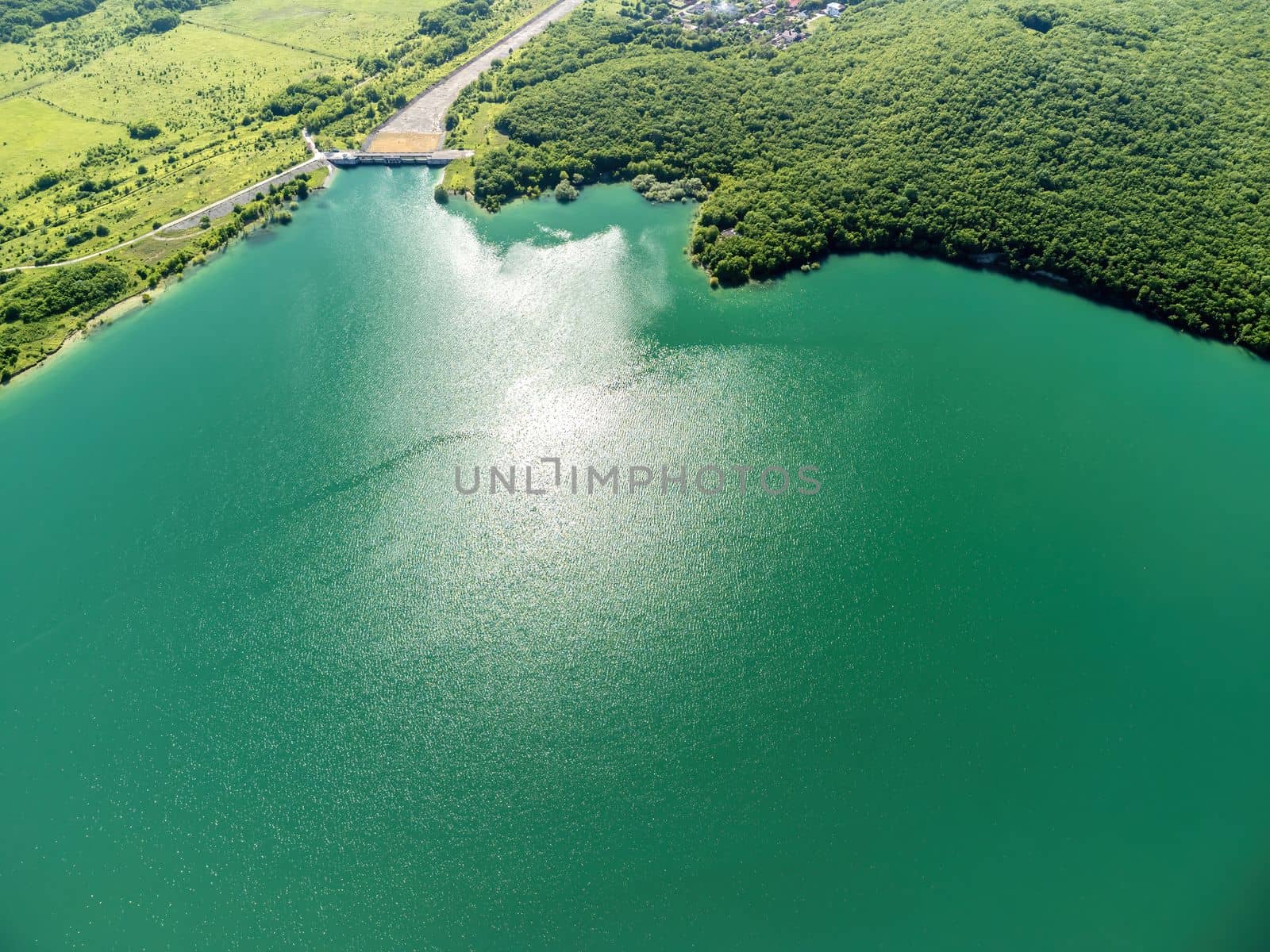 Aerial landscape from flying drone storage reservoir at mountain foot covered colorful spring forest. Beautiful view from above blue lake among highlands