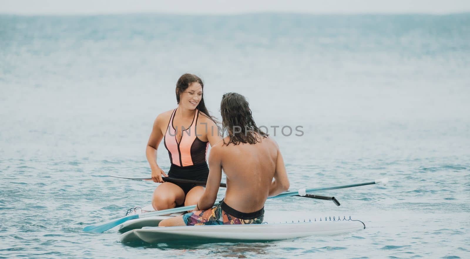 Sea woman and man on sup. Silhouette of happy young woman and man, surfing on SUP board, confident paddling through water surface. Idyllic sunset. Active lifestyle at sea or river