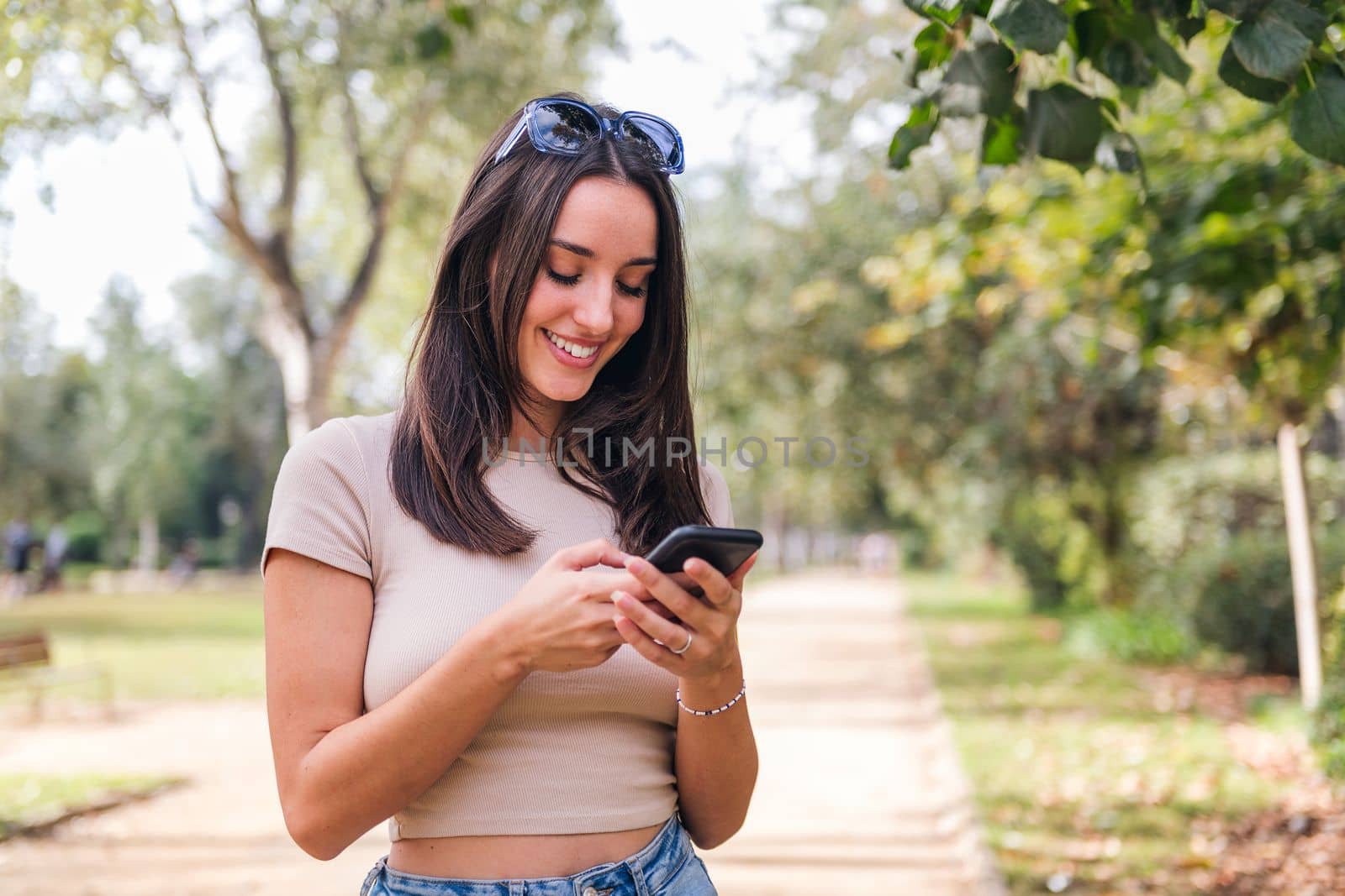 smiling young caucasian woman typing on her mobile phone in a park, concept of youth and technology of communication