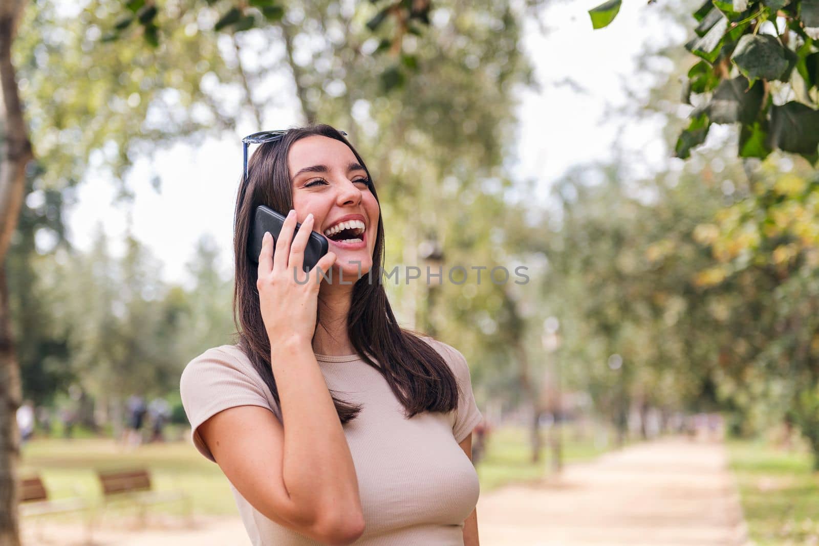 young caucasian woman laughing during a call with her mobile phone in a park, concept of youth and technology of communication, copy space for text