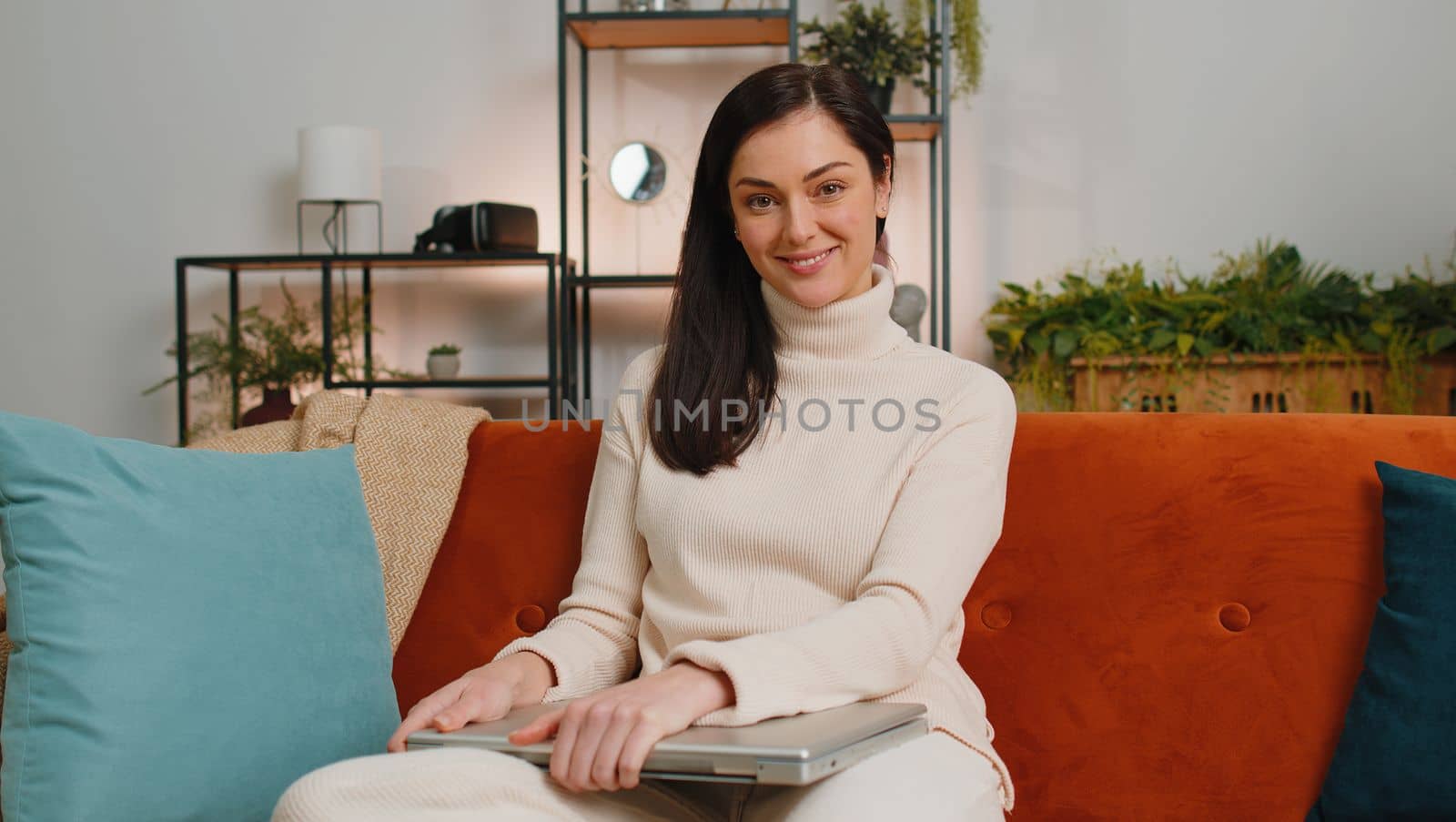 Young woman using credit bank card and laptop computer while transferring money, purchases online shopping, order food delivery at home apartment. Adult girl in day living room sitting on couch indoor