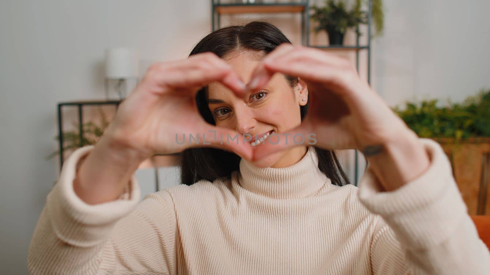 I love you. Happy brunette woman at home living room couch makes symbol of love, showing heart sign to camera, express romantic feelings express sincere positive feelings. Charity, gratitude, donation