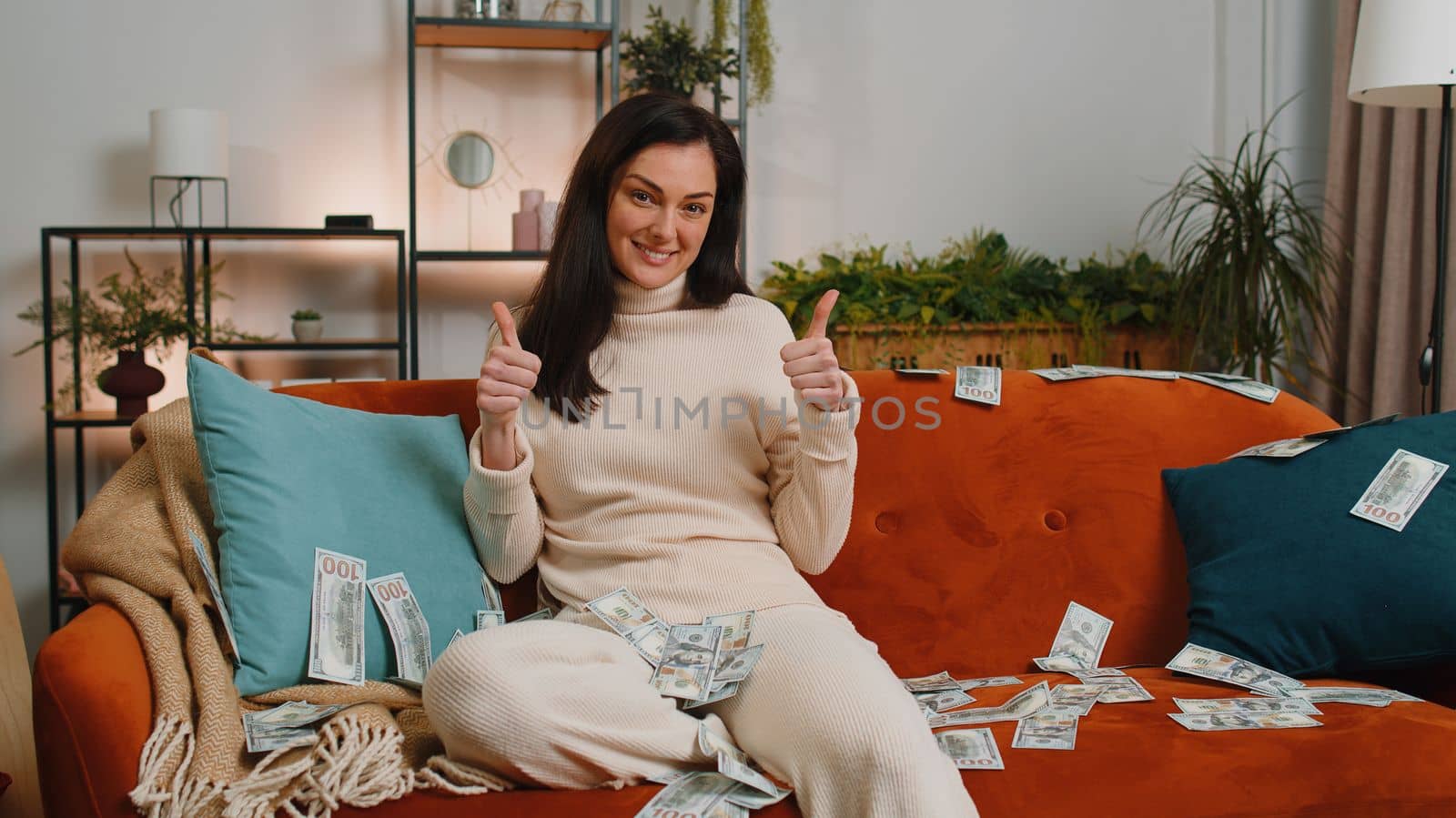 Successful happy rich business woman counting money cheering up with high profits, lottery game win, satisfied of wealth income earnings salary. Girl at home room couch full of dollar cash banknotes