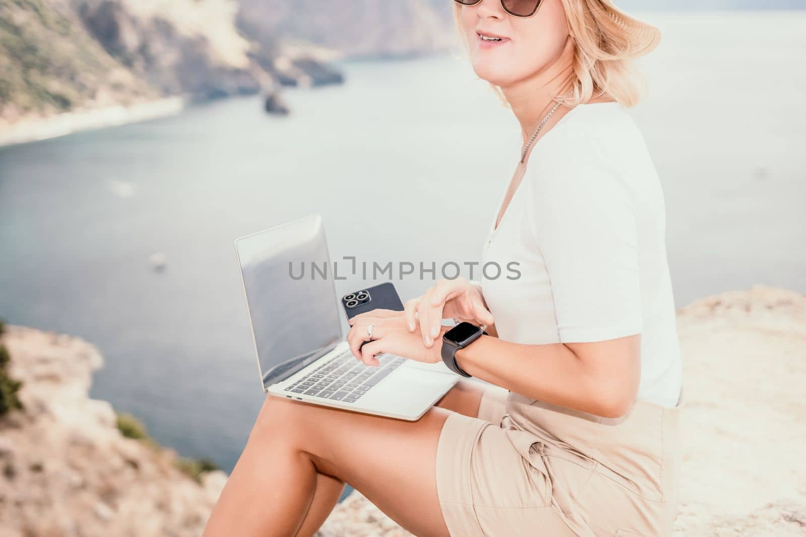 Digital nomad, Business woman working on laptop by the sea. Pretty lady typing on computer by the sea at sunset, makes a business transaction online from a distance. Freelance, remote work on vacation by panophotograph