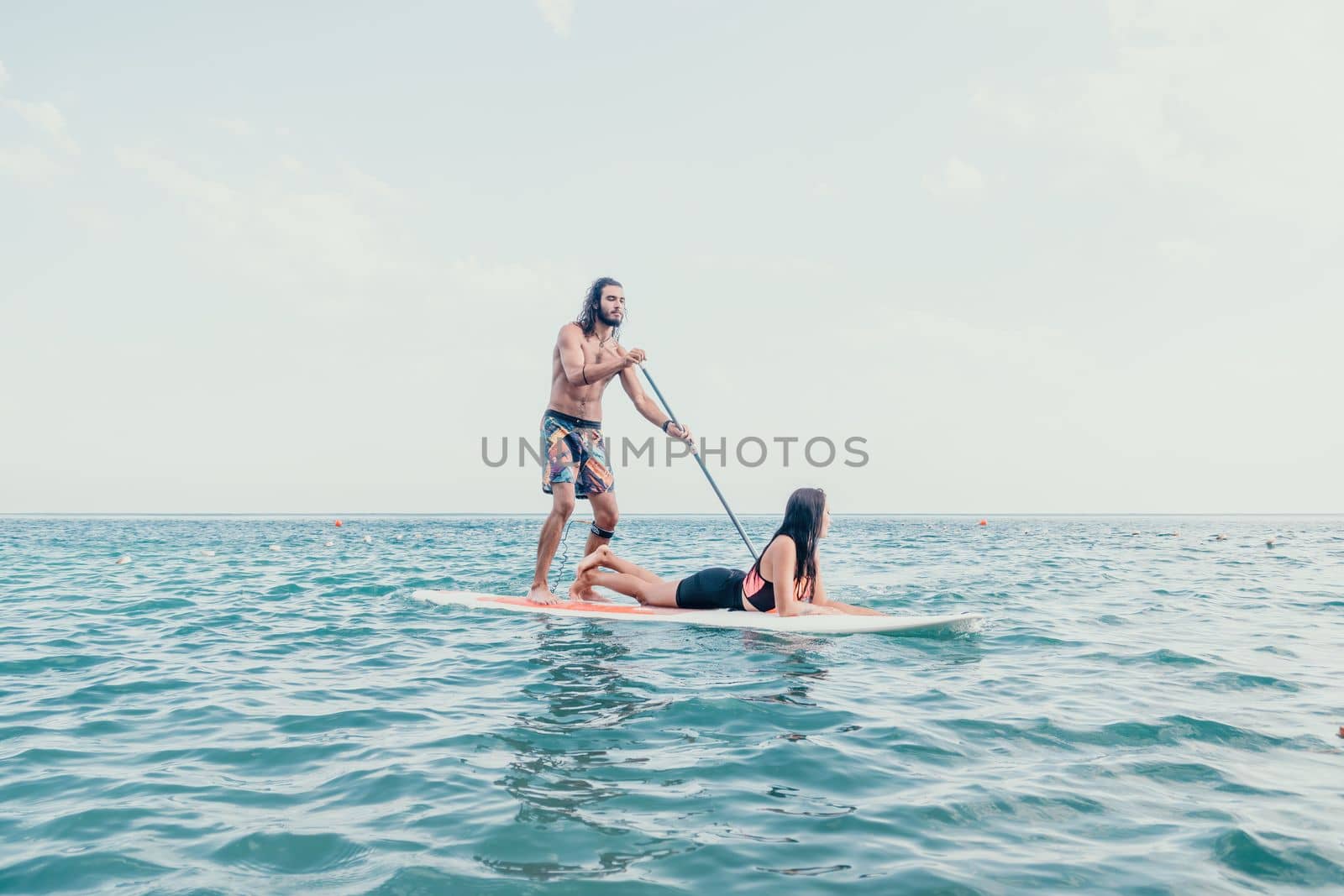 Sea woman and man on sup. Silhouette of happy young woman and man, surfing on SUP board, confident paddling through water surface. Idyllic sunset. Active lifestyle at sea or river. by panophotograph