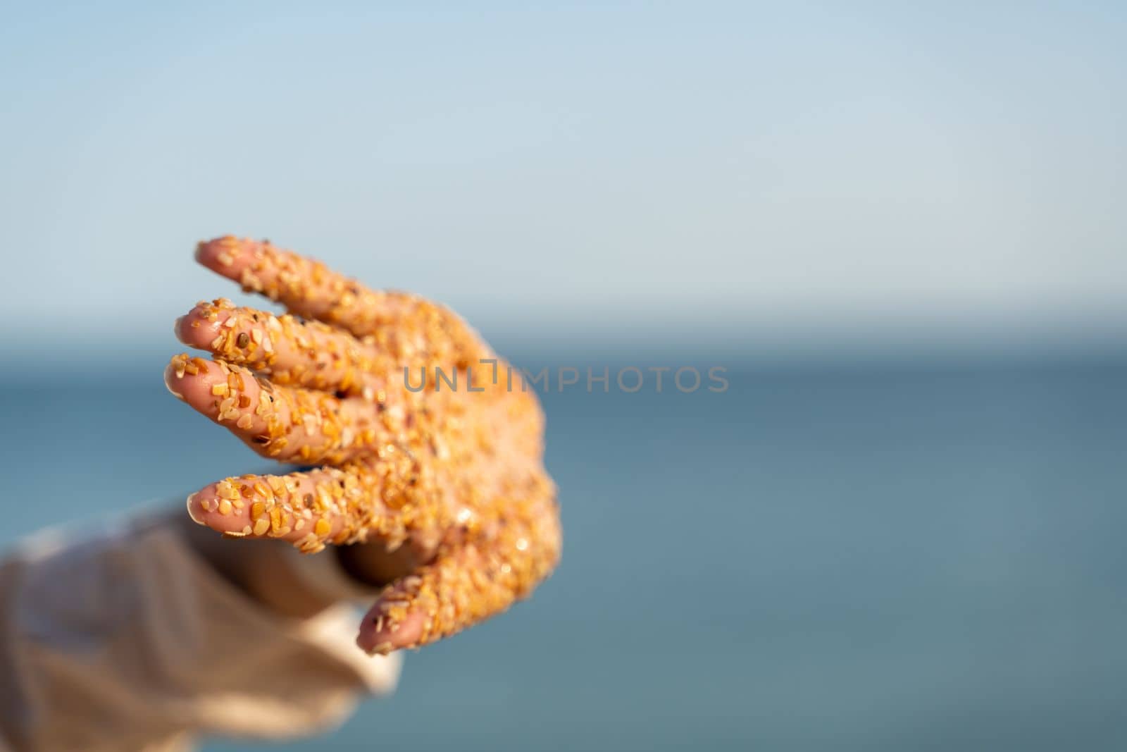 Sand hand sea. Small pieces of shells sand stuck to the palms of a woman against the backdrop of the sea and blue sky. by Matiunina