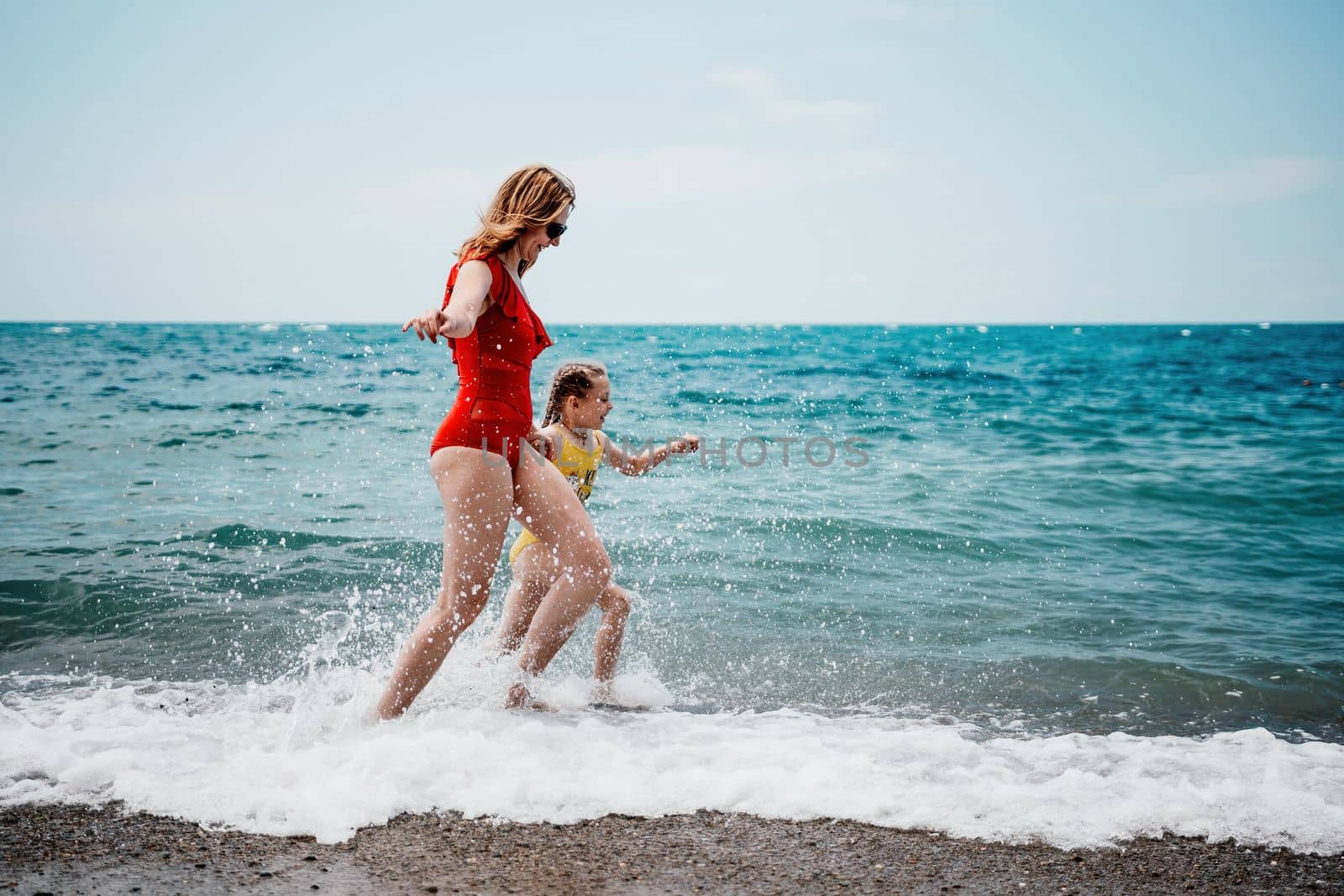 Happy loving family mother and daughter having fun together on the beach. Mum playing with her kid in holiday vacation next to the ocean - Family lifestyle and love concept.