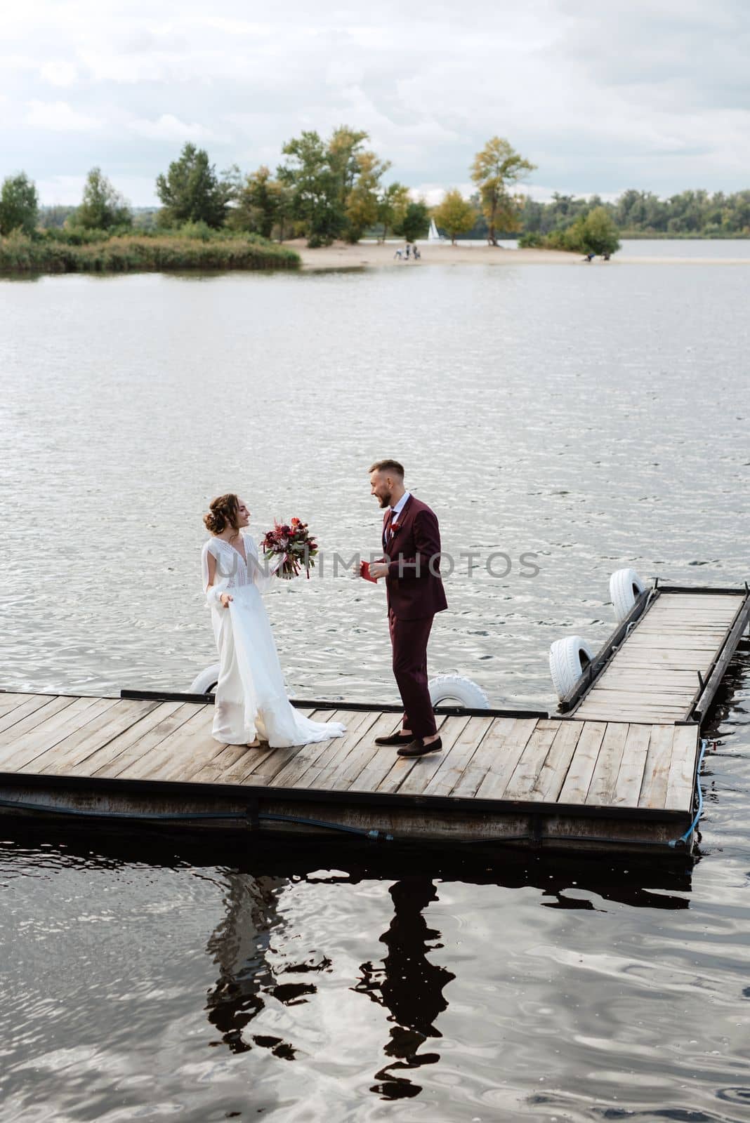 the first meeting of the bride and groom in wedding dresses on the pier near the water