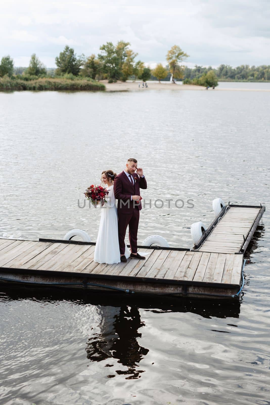 the first meeting of the bride and groom in wedding dresses on the pier near the water