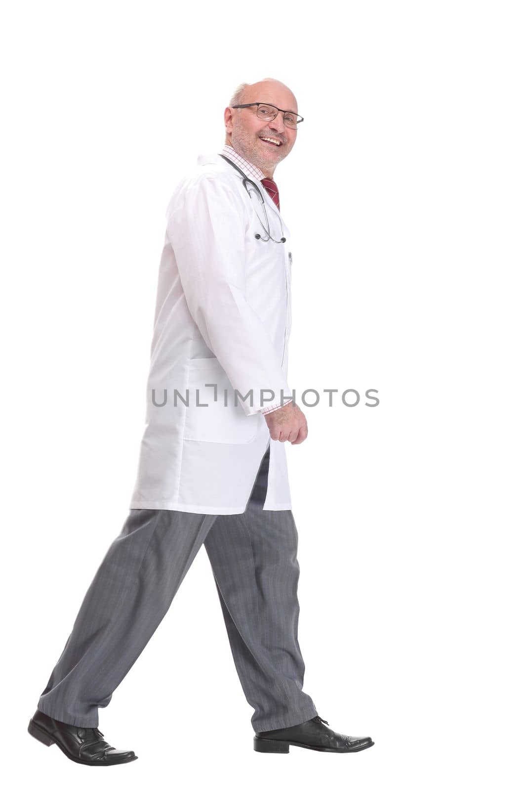 Mature doctor with stethoscope walking on white background, side view