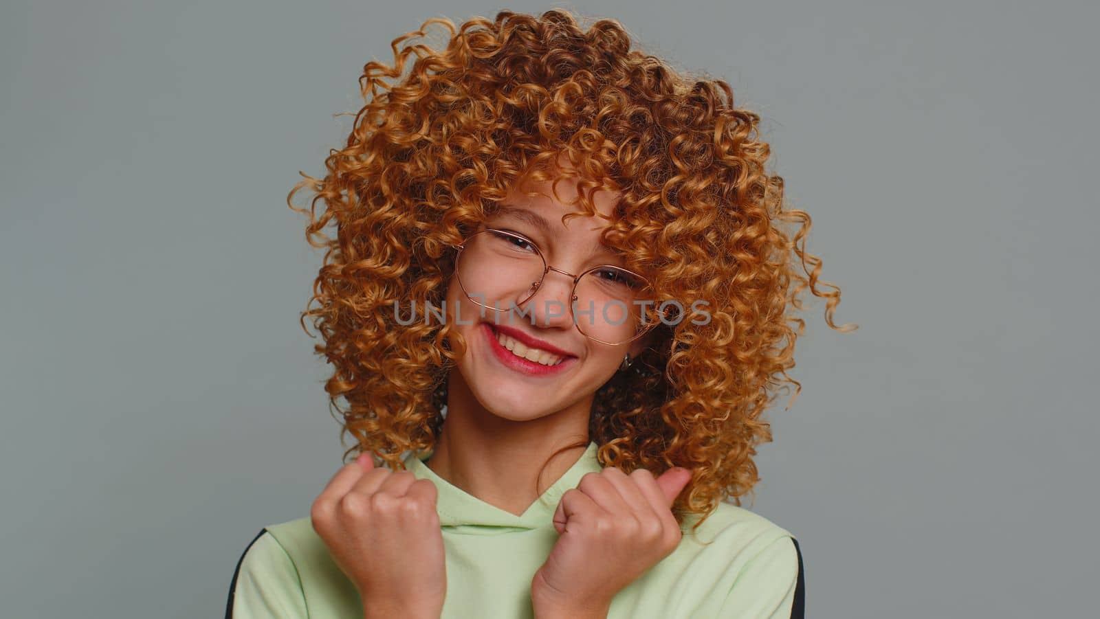 Young child girl kid shouting, raising fists in gesture I did it, celebrating success, winning, birthday, lottery jackpot goal achievemen. Teenager children with curly hair isolated on gray background