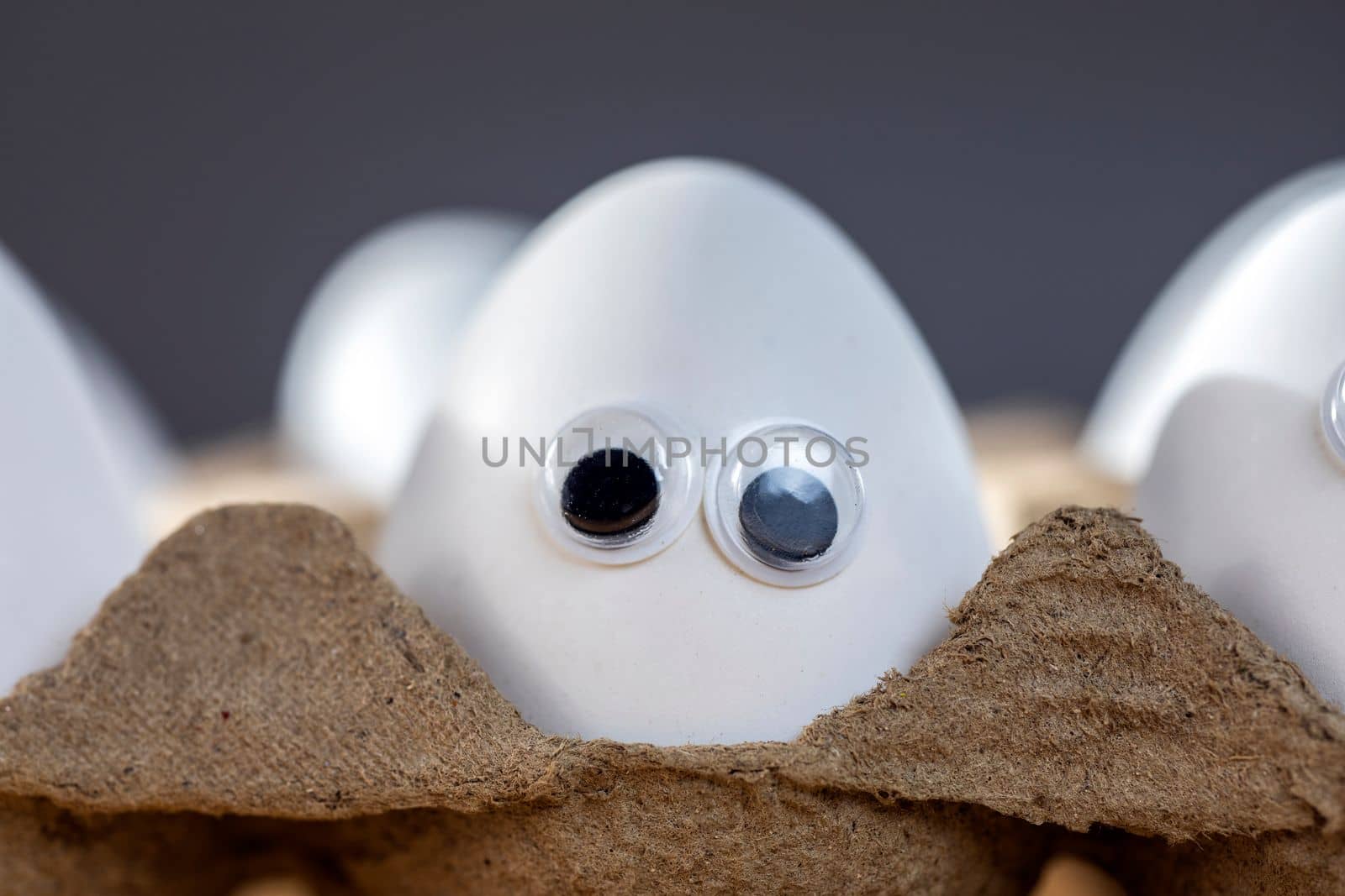 Funny faces on white eggs in carton box with organic chicken eggs on kitchen table closeup big animation eyes. humor, food and easter holiday concept. close up