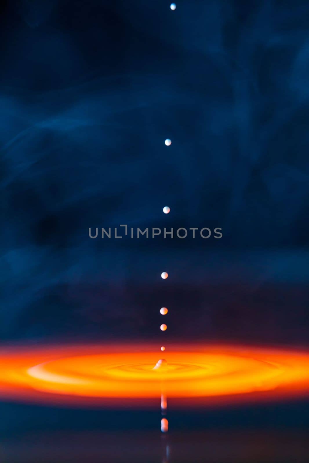 The drop falls into a thick liquid with a blue-yellow background in the smoke. Abstract colorful background