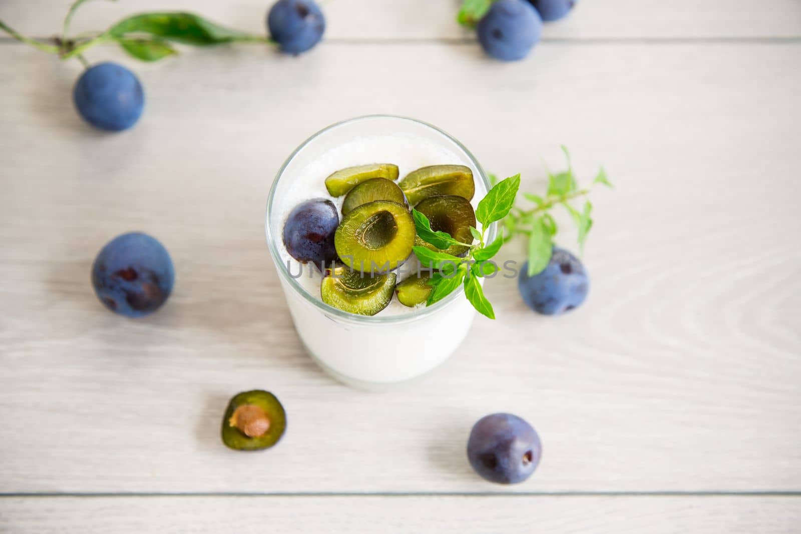 sweet homemade yogurt with fresh plum slices in a glass on a wooden table