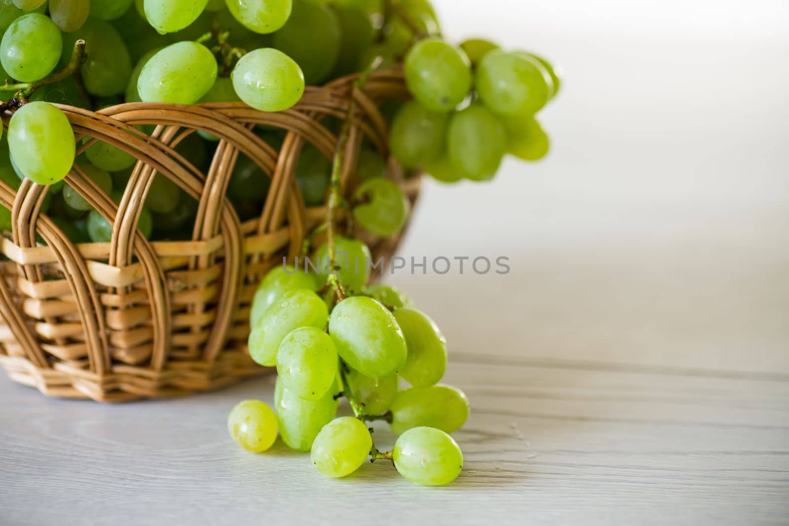 green autumn ripe grapes in a basket on a light wooden table
