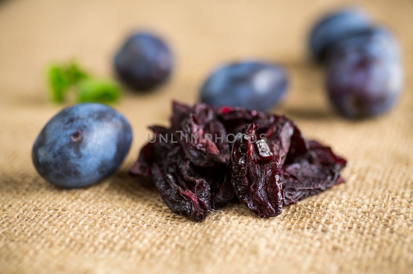 Dried prunes in a spoon on a burlap tablecloth against a background of fresh plums. Prunes and plums on a kitchen table close-up.