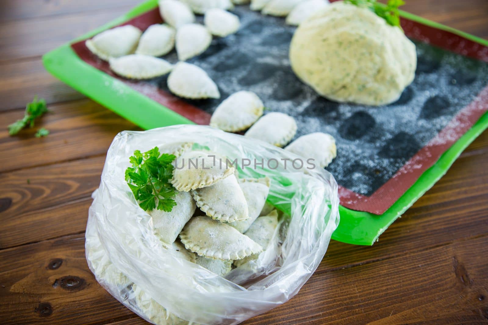 Raw green dough dumplings with parsley, dill. Raw dumplings in a bag on a wooden table.