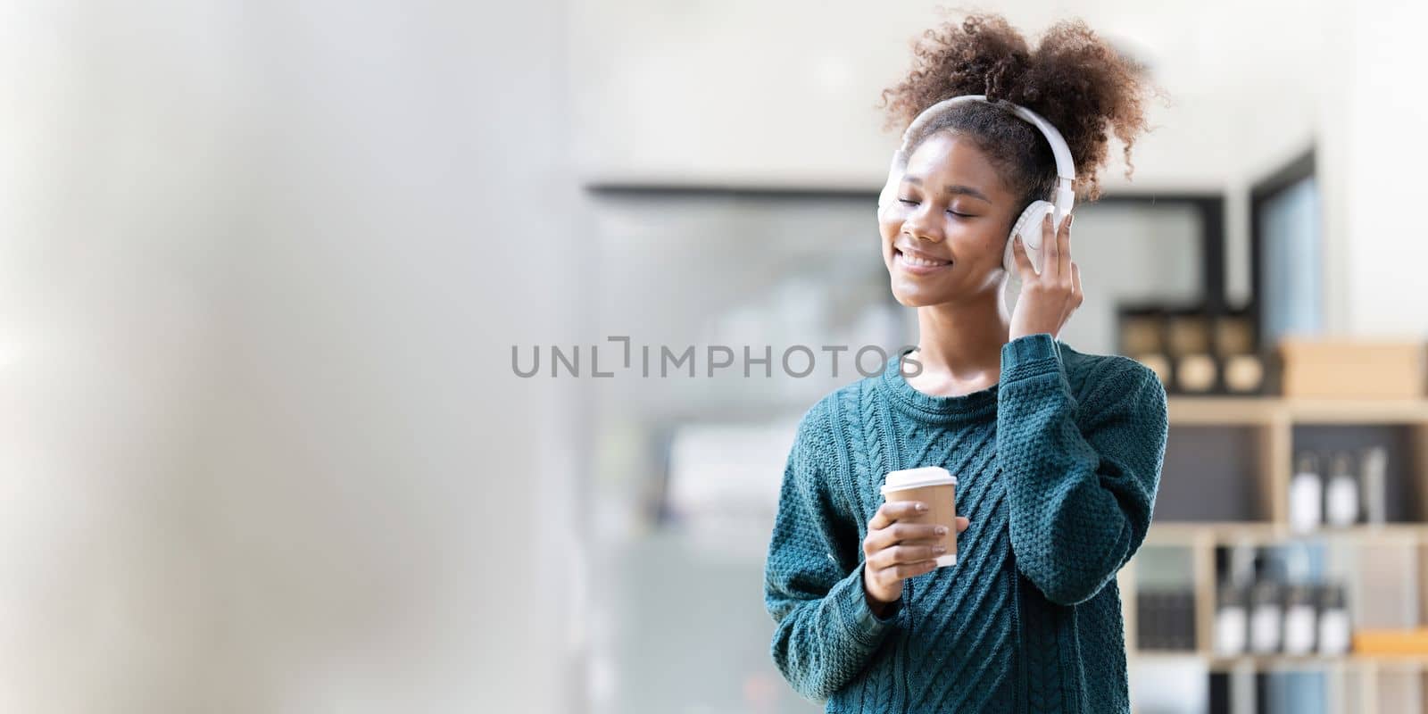 Young woman resting comfortably listening to music and holding a cup of coffee at home.