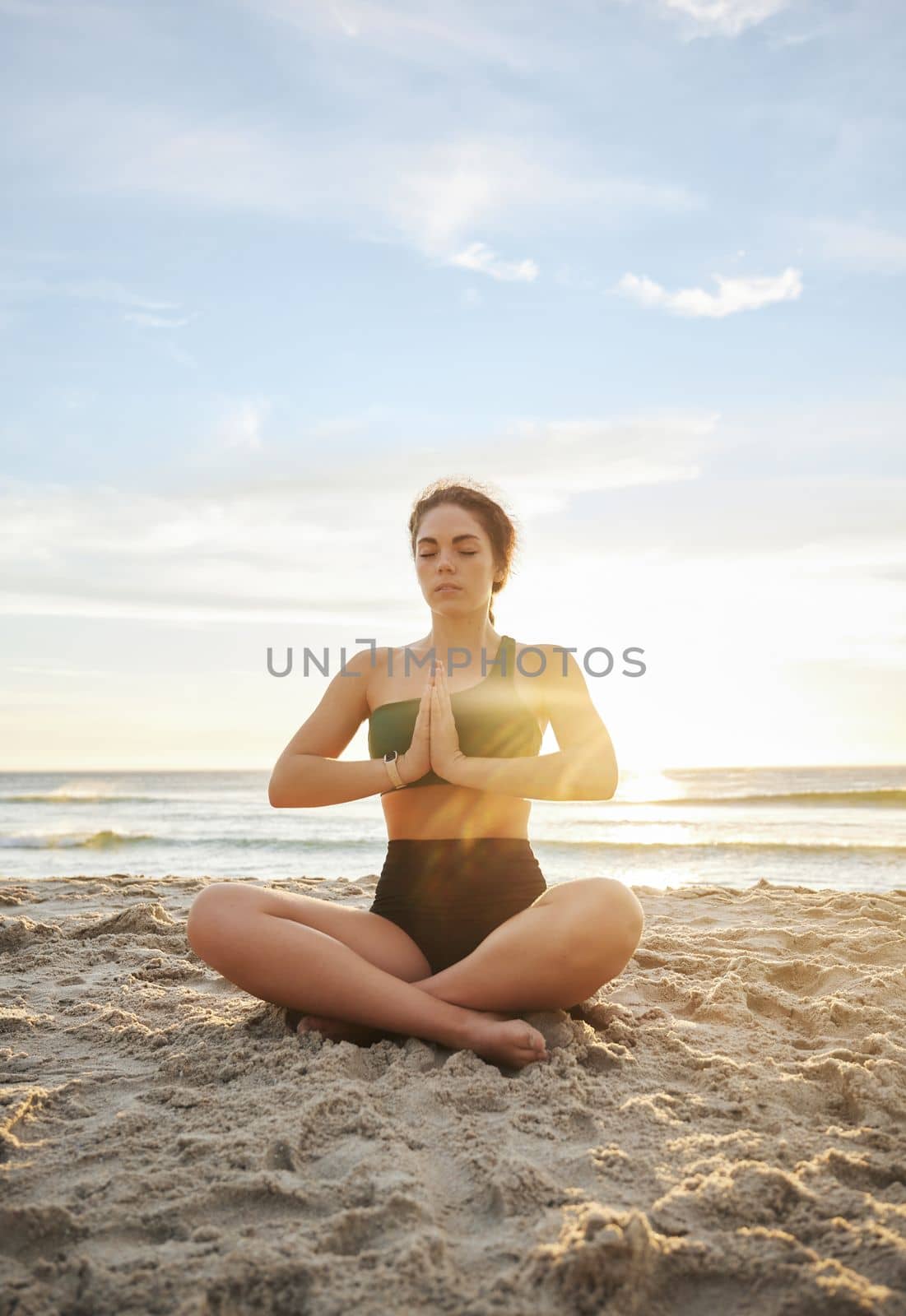 Woman, yoga and meditation on the beach in namaste for spiritual wellness or zen workout in the sunset. Female yogi relaxing and meditating for calm, peaceful mind or awareness by the ocean coast.