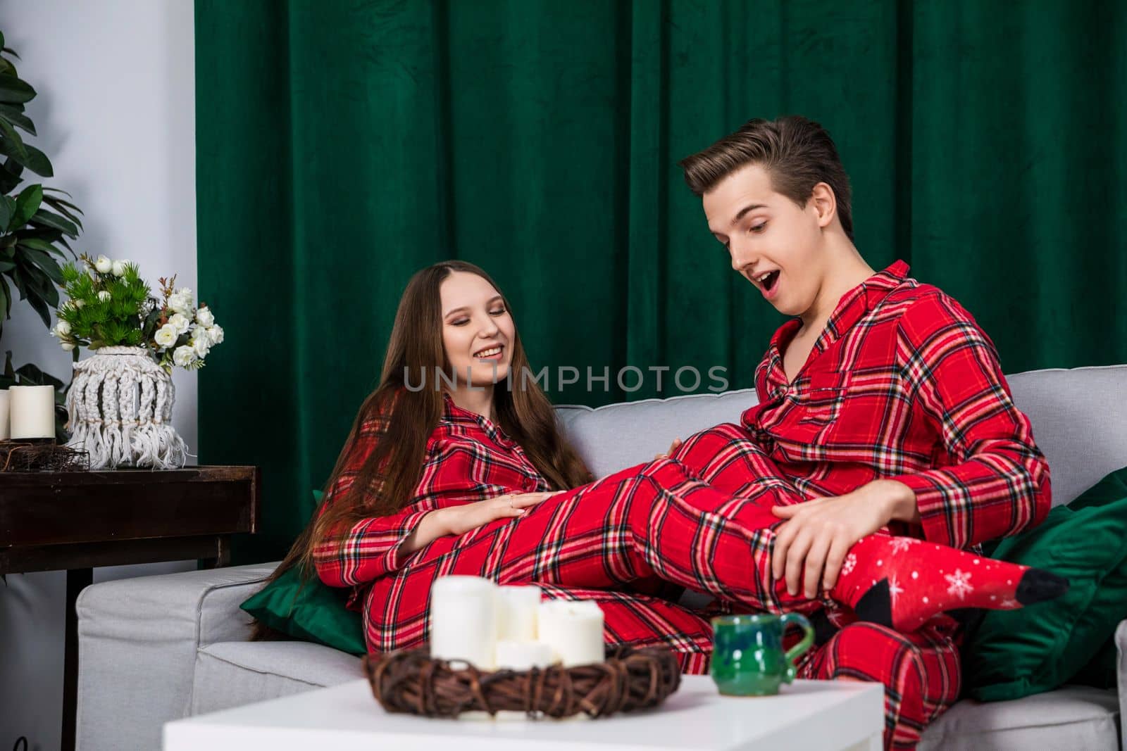 Girl and boy dressed in identical pajamas pose for a photo shoot. Photo session of a couple in love. Romantic photos of a man and a woman against the background of a green curtain.