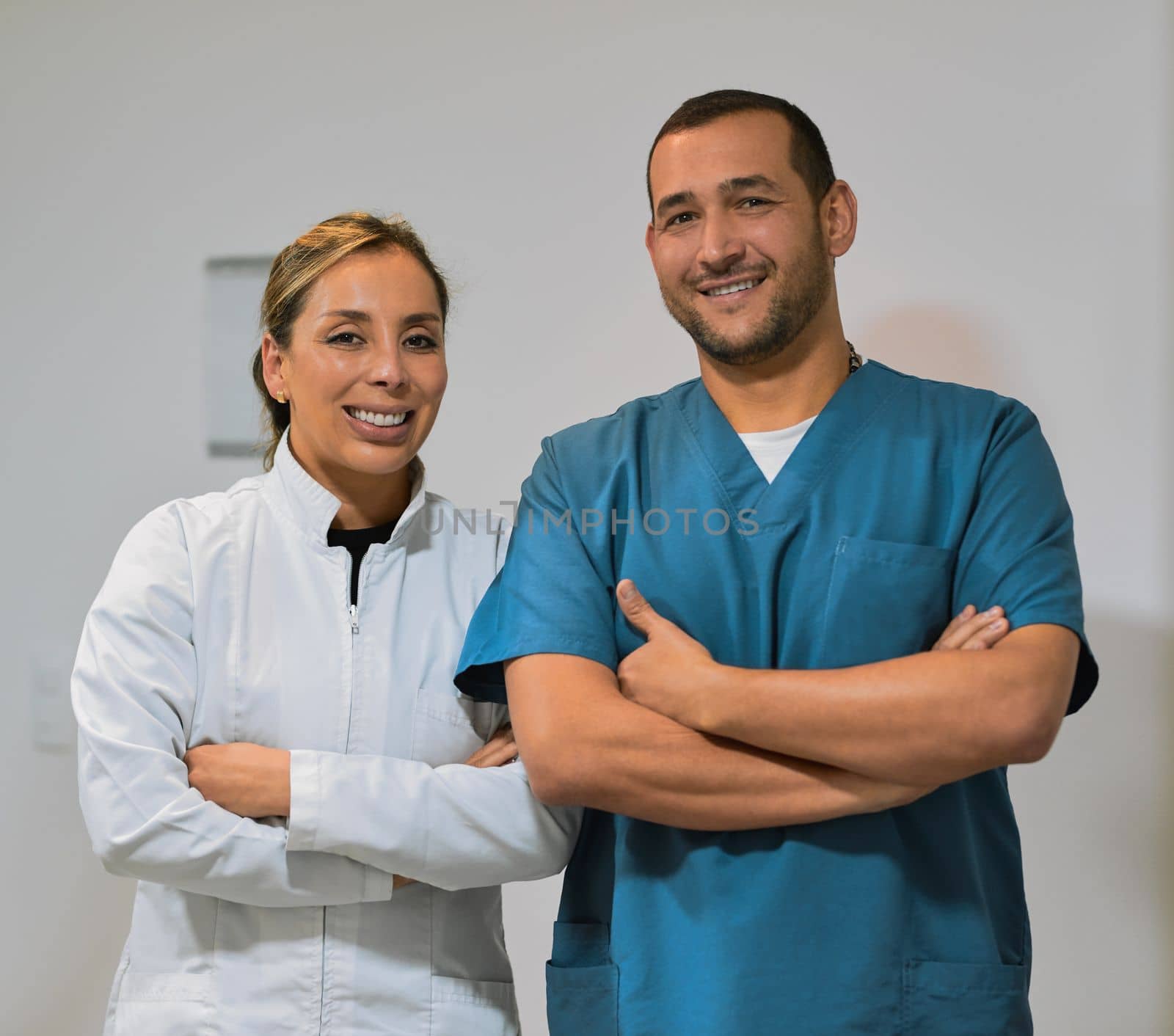 They will take care of all your tooth related problems. two confident young dentists standing with arms folded while looking into the camera inside the office. by YuriArcurs